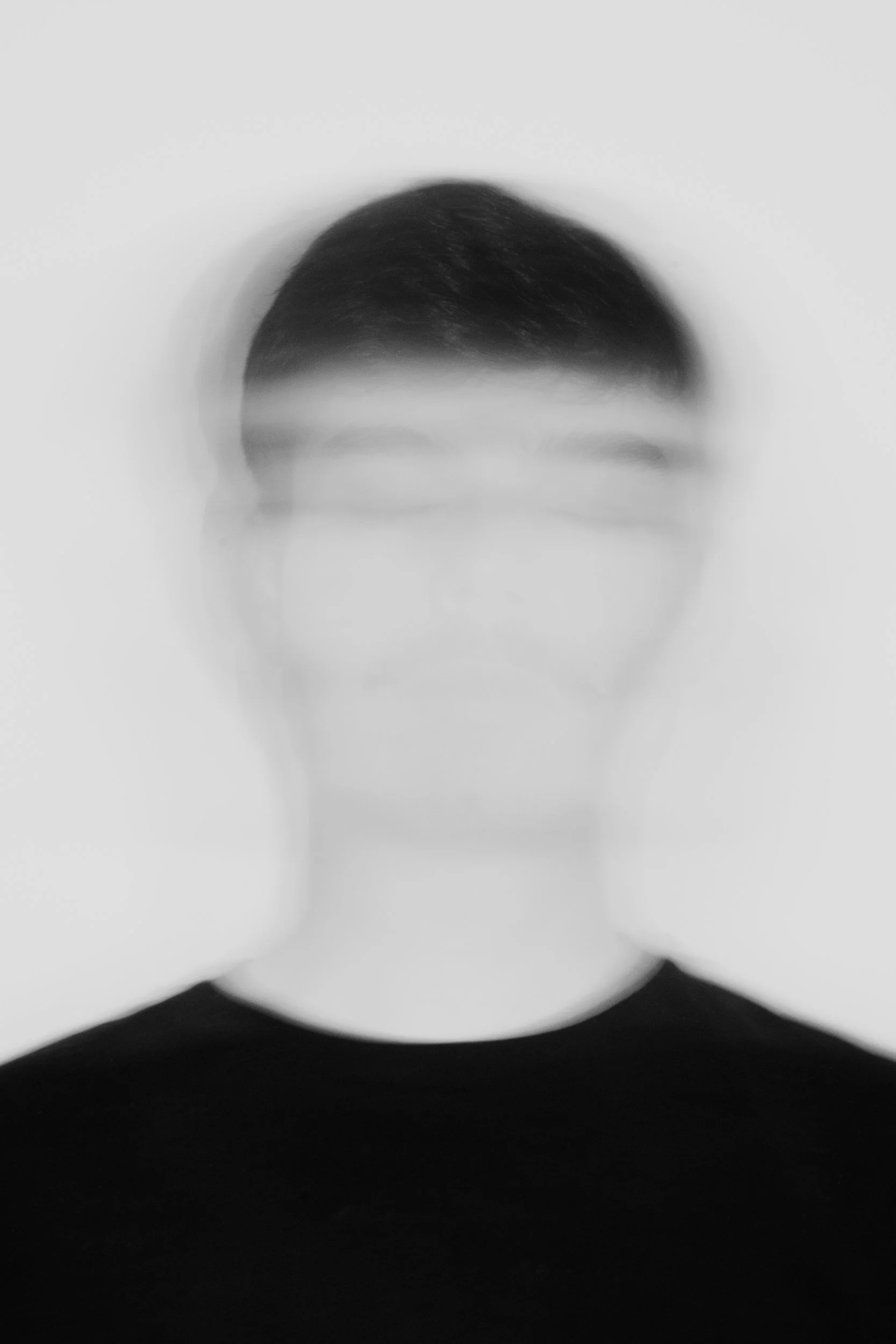 A black-and-white photo of a person with short hair, wearing glasses, and a black shirt, with a blurred effect.