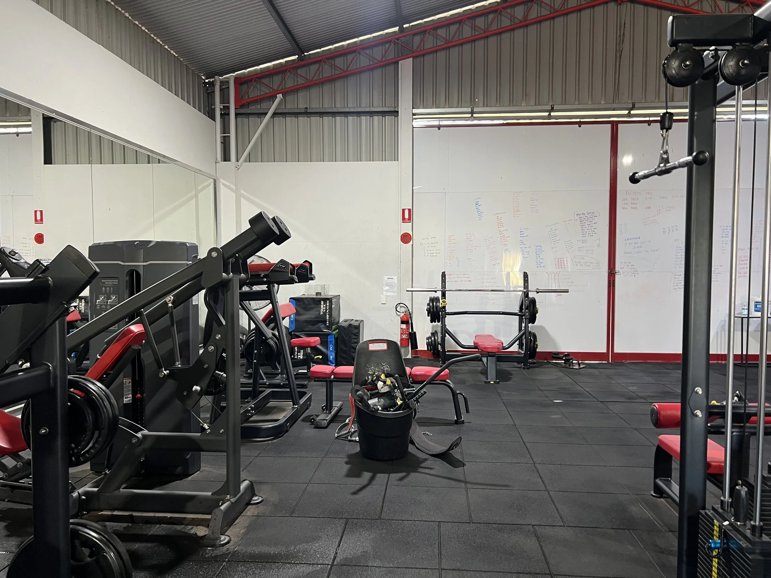 Empty gym with weightlifting equipment, benches, weights, and a whiteboard with writing on the wall. commercial cleaning western nsw