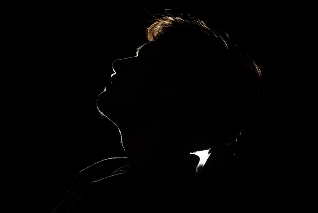 Silhouette of a woman and a man with their faces close, backlit to create a dramatic profile view against a black background.