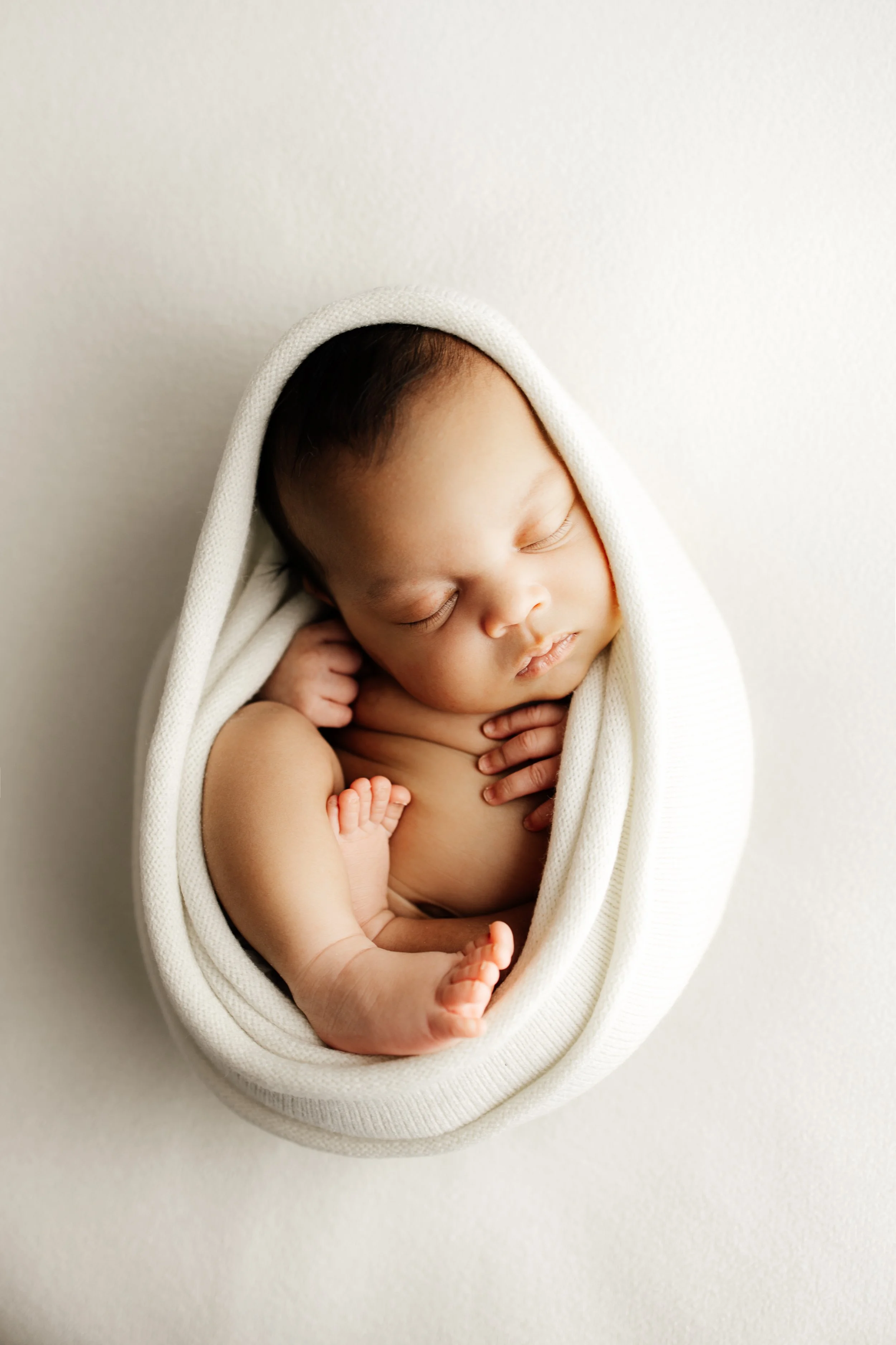 Un bébé endormi dans une couverture blanche, les yeux fermés, avec un fond blanc