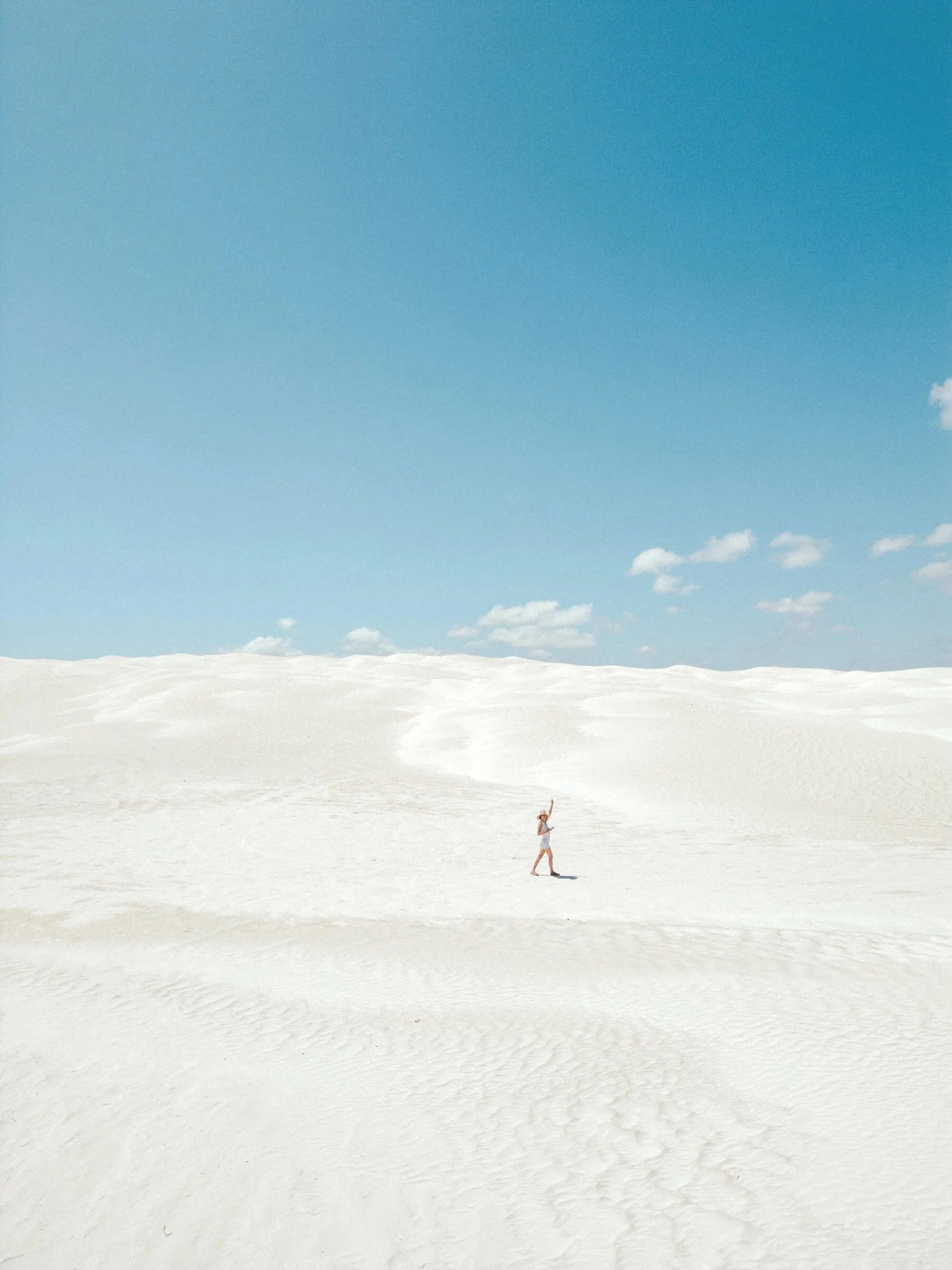 A person walking in a vast white sandy desert landscape with a clear blue sky above.