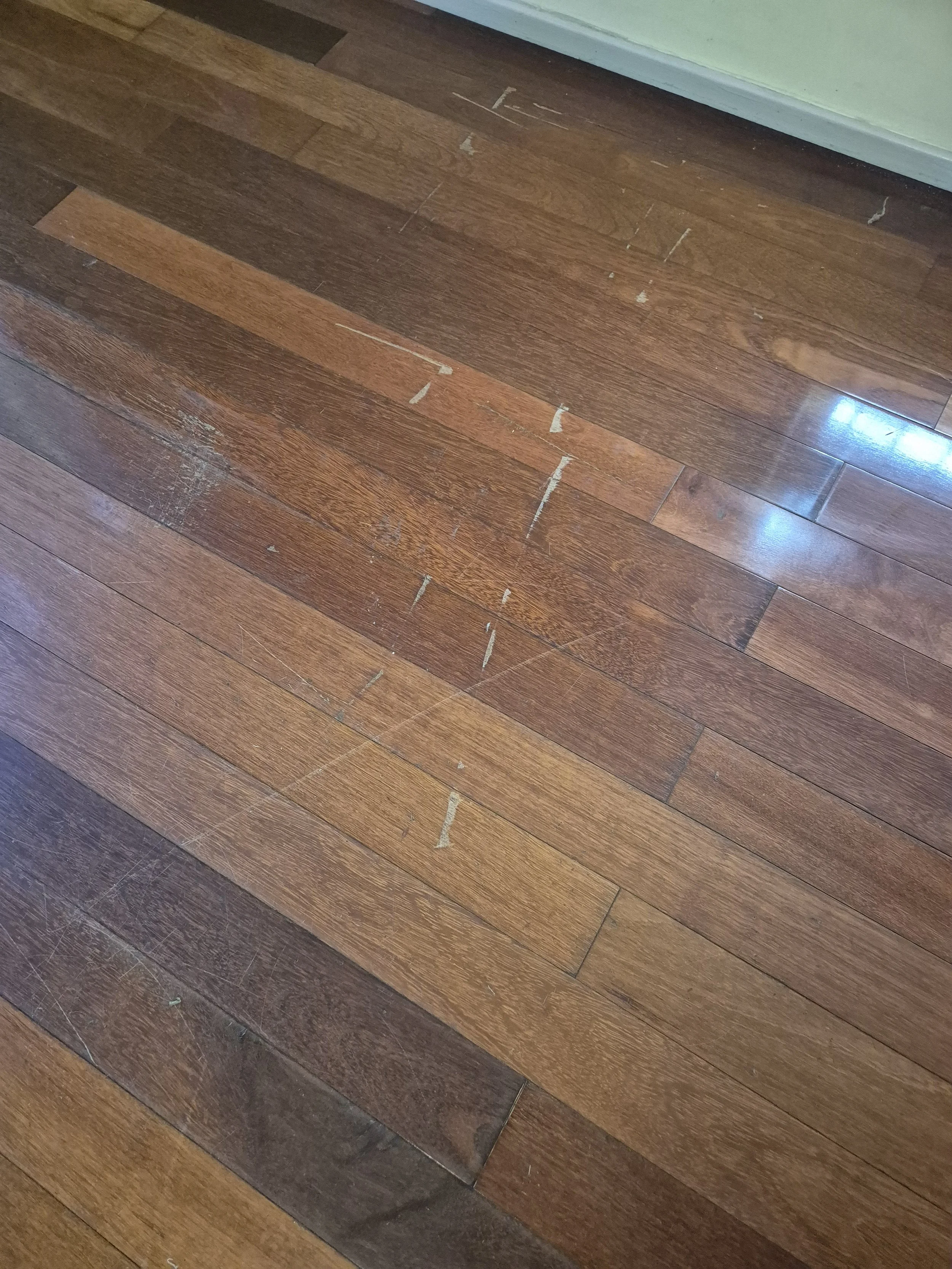 Wooden floor with some scratches, scuffs, and paint marks near a green wall.