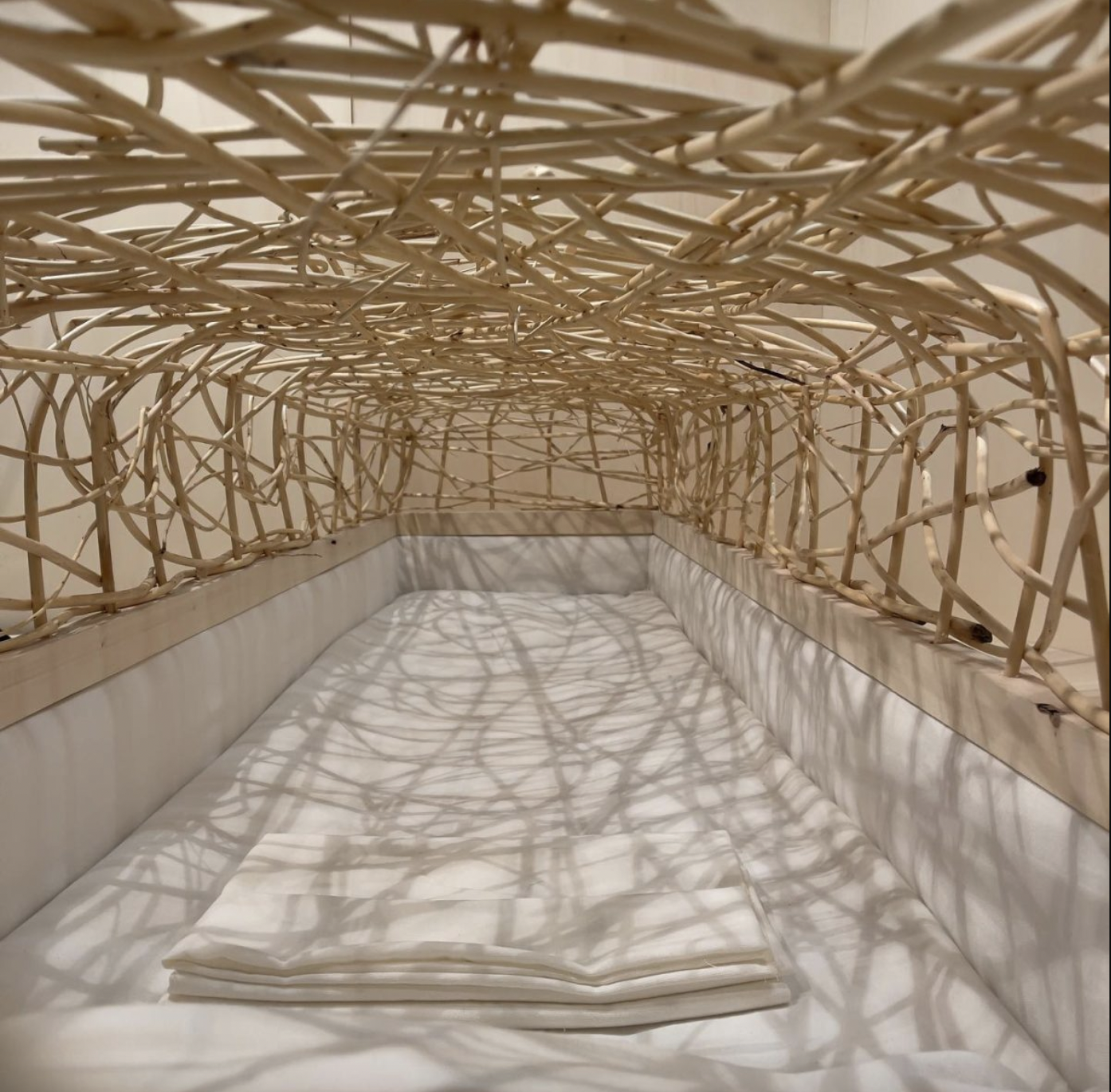 Een bed met een houten frame dat uit dunne, vertakte takken of riet bestaat, waardoor er ingewikkelde schaduwen op het witte beddengoed ontstaan.