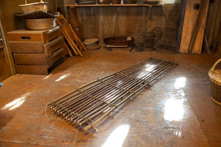 Een houten winkelwagentje op een houten vloer, met houten planken en manden op de achtergrond, in een rustieke opslagruimte.