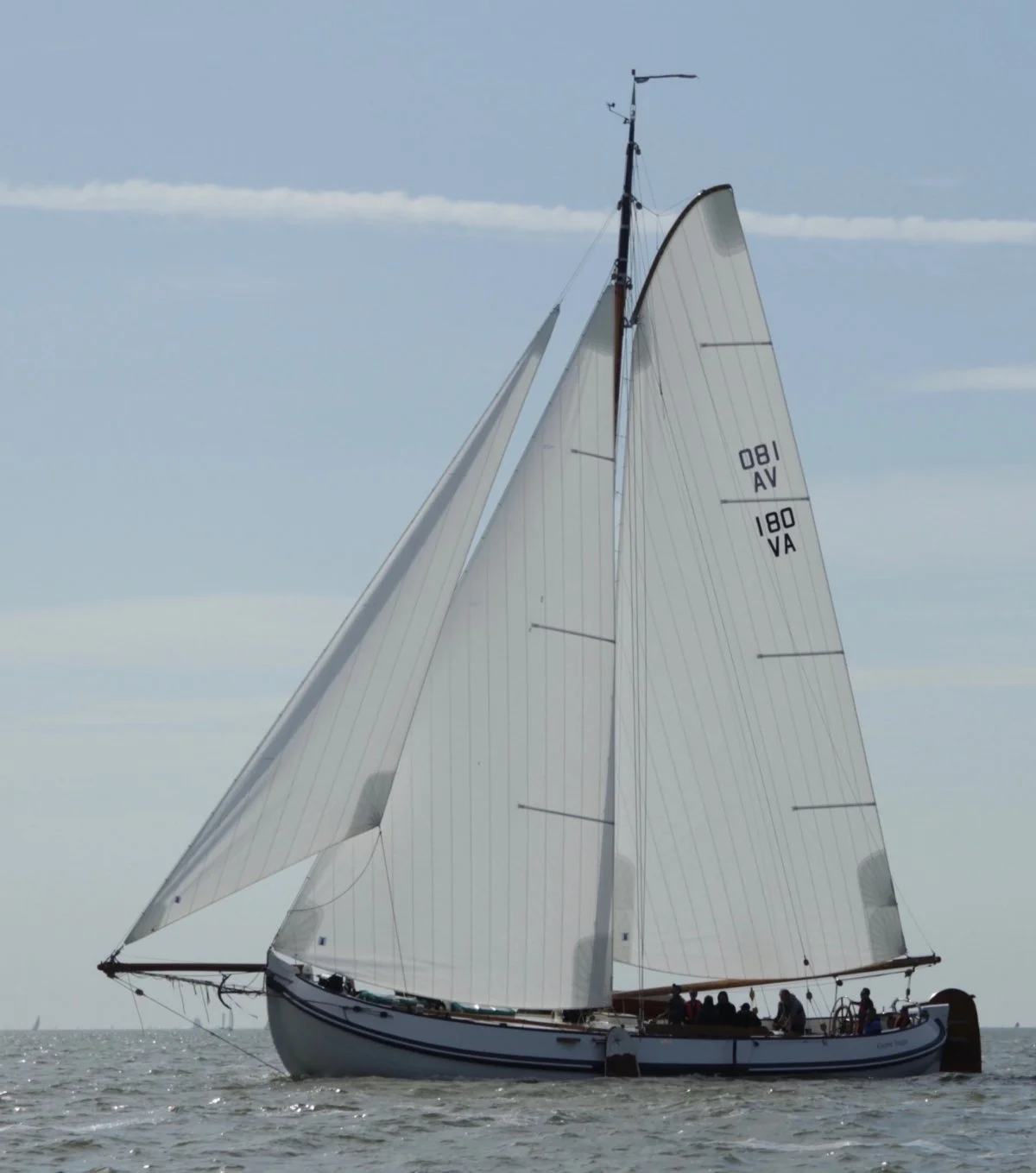 Een zeilboot met witte zeilen vaart op de oceaan, met mensen aan dek.