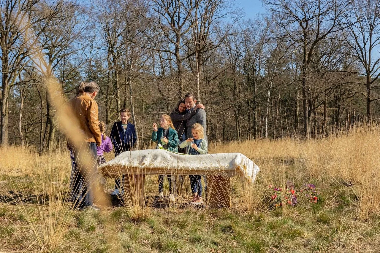 Een groep mensen die afscheid neemt op een openlucht locatie, omringd door gras en bomen.