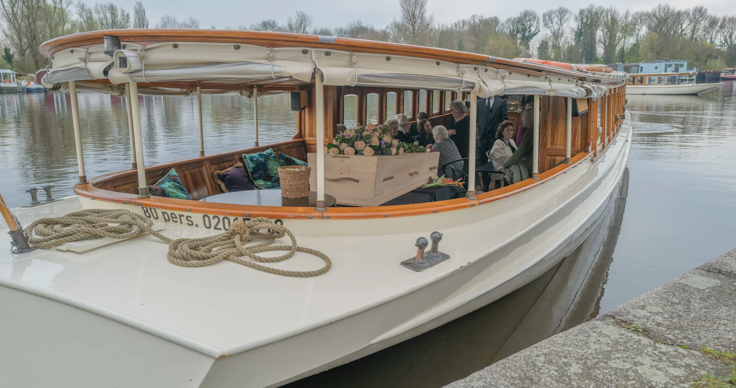 Mobiele boot met een groep mensen binnen die een feest of bijeenkomst houden, met bloemen en decoraties, aangemeerd aan een kade.