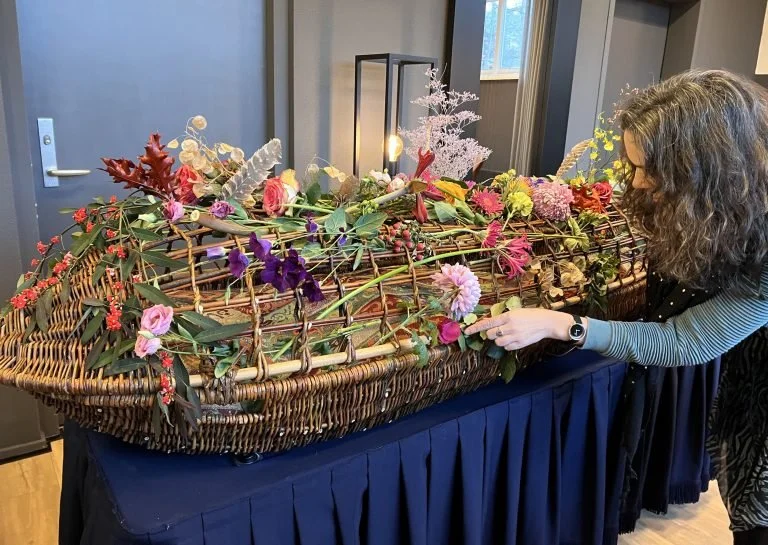 Een vrouw die bloemen plaatst op een bloemstuk in een uitschuifbare lijkkist.