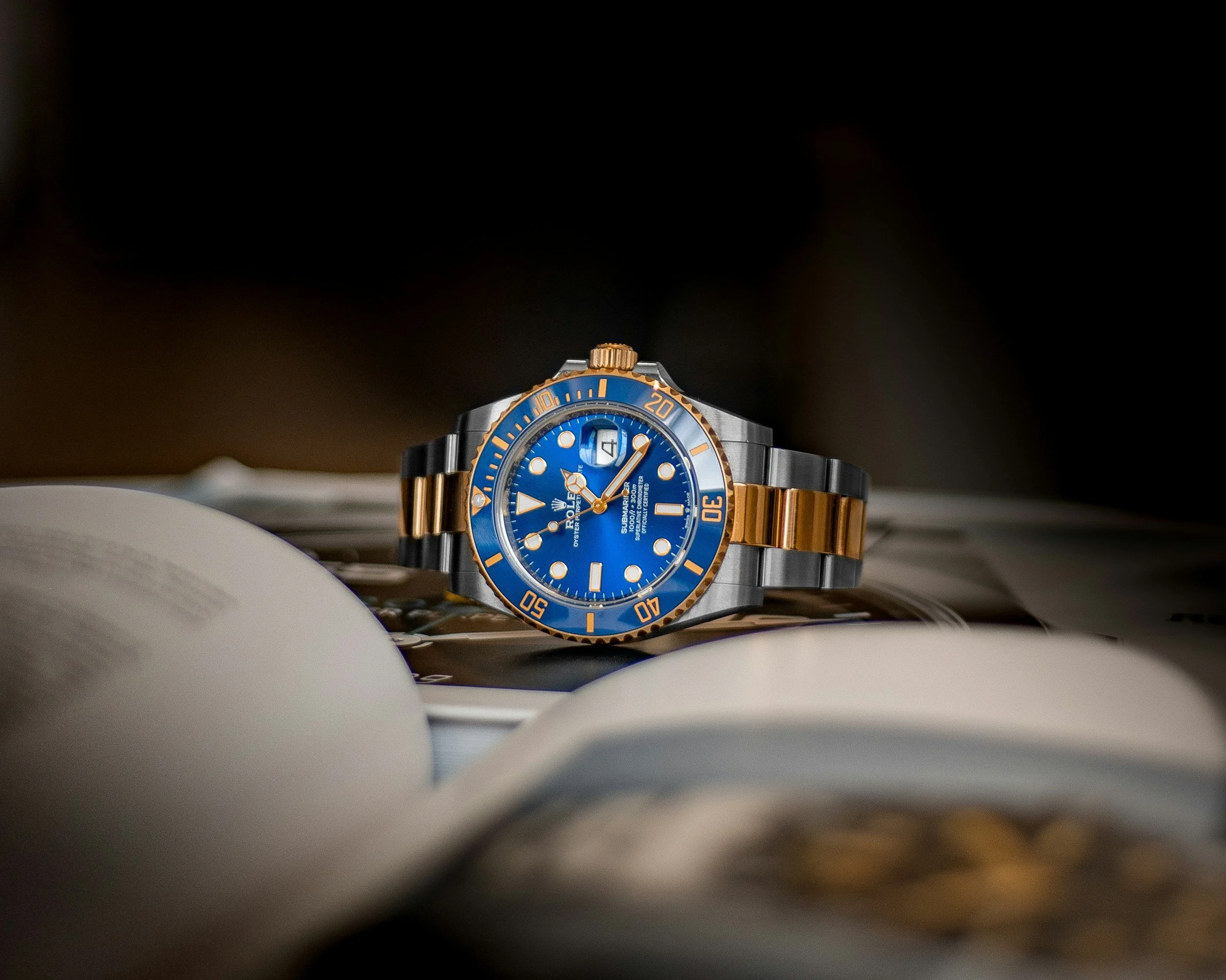 A luxury watch with a blue dial, gold accents, and a black and gold metal strap, resting on open magazines.