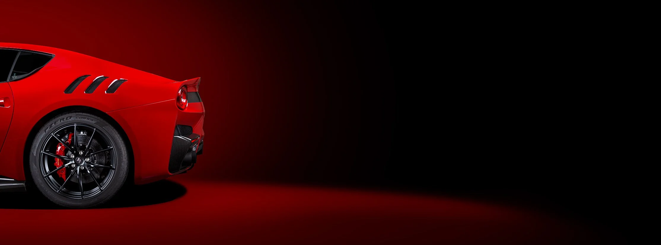 Partial view of a red sports car with black wheels and black vents, set against a dark background.