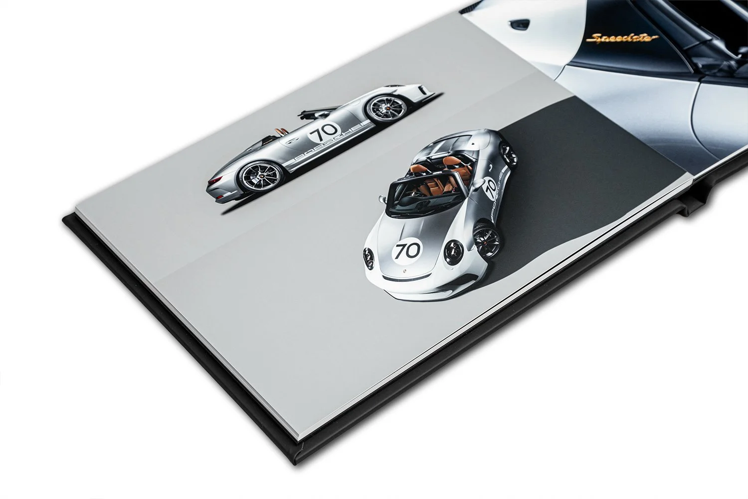 Open book showing two Porsche sports cars, one silver and one white, both with the number 70 on their hoods, on a plain background.