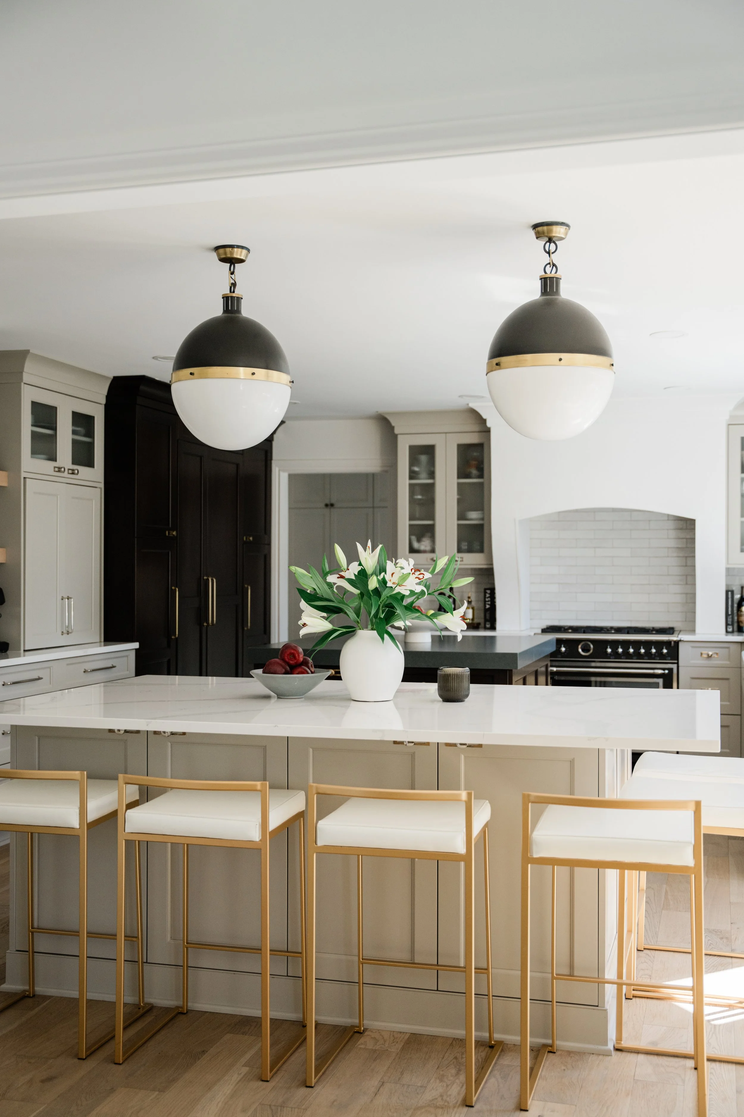 Modern kitchen with white island, black and white cabinetry, and two black pendant lights hanging from ceiling.