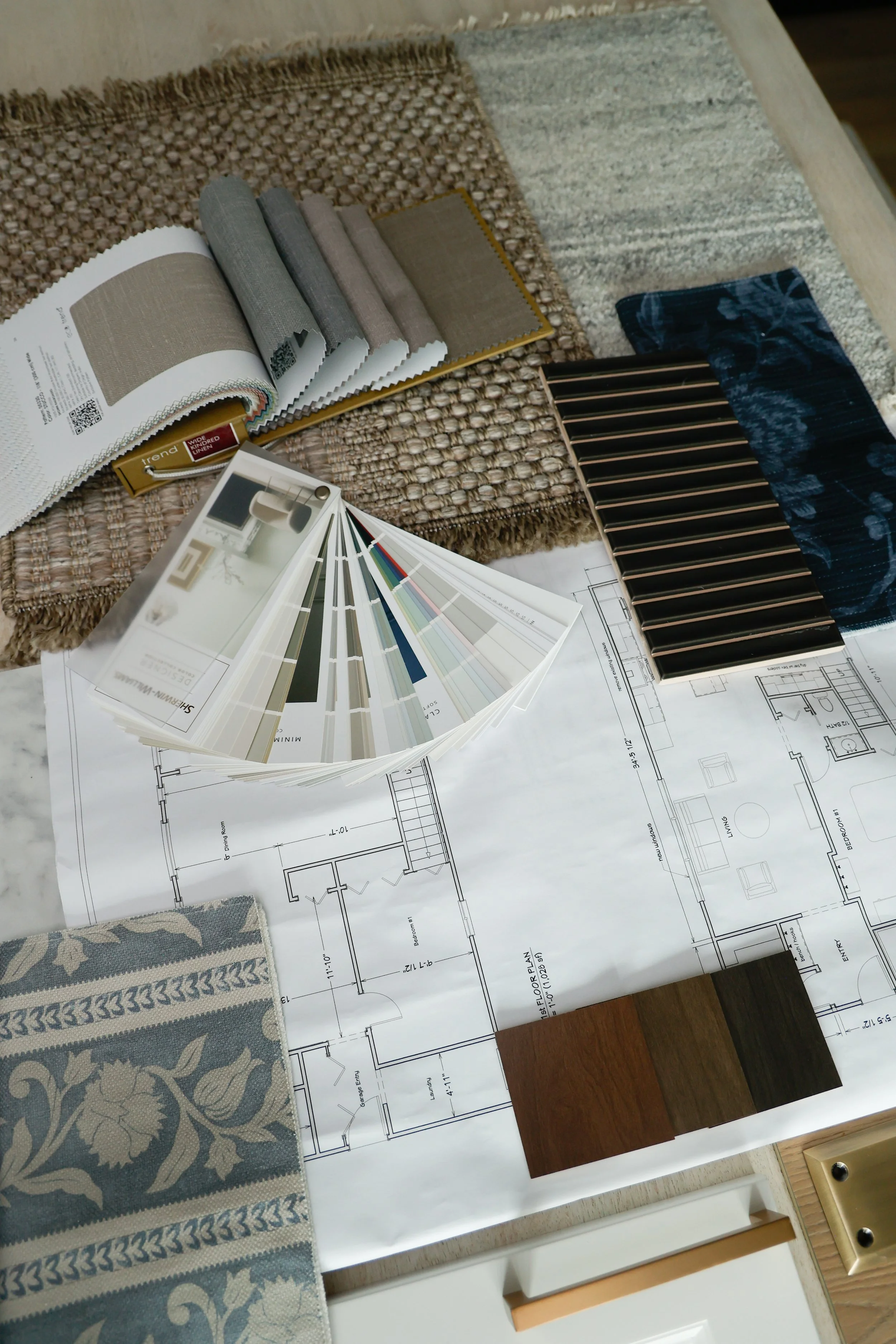 Sample of interior design materials including fabric swatches, paint color samples, and floor plans on a table.