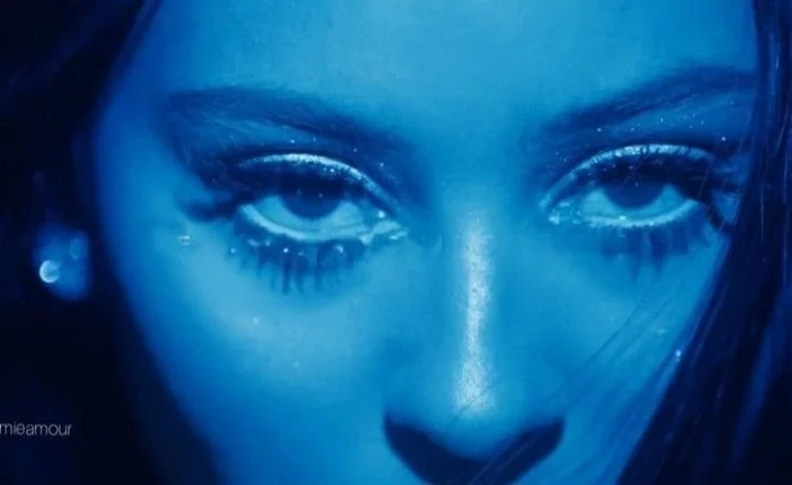 Close-up of a woman's face with makeup, heavily focused on her eyes and nose, in a blue-toned photo.