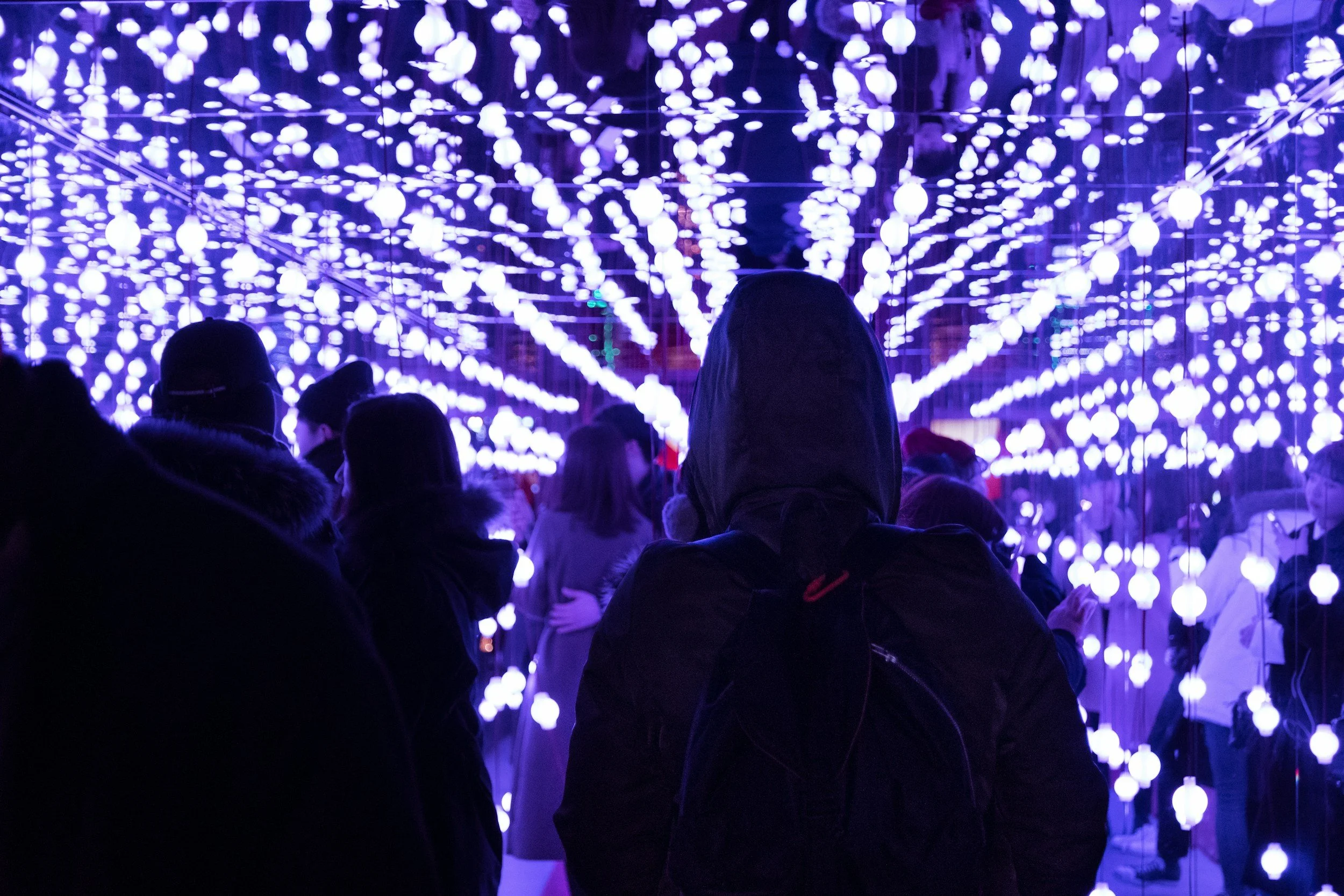 People standing under a ceiling of numerous glowing purple and white lights in a dark indoor space.