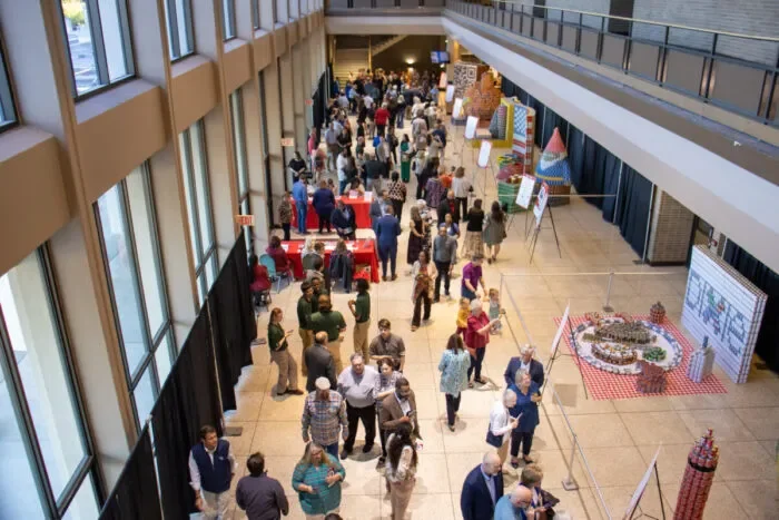 People attending a public event or exhibition in a large indoor space with tables and displays.