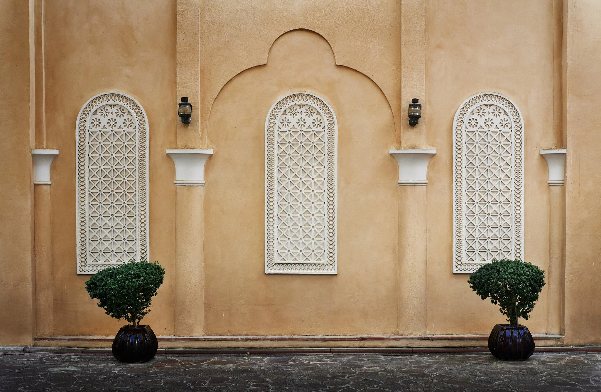 Symmetrical architectural shot of a traditional Qatari building facade in Doha, featuring ornate white window screens (mashrabiya), arched details, and minimalist landscaping. Photography by Pedro Ferr