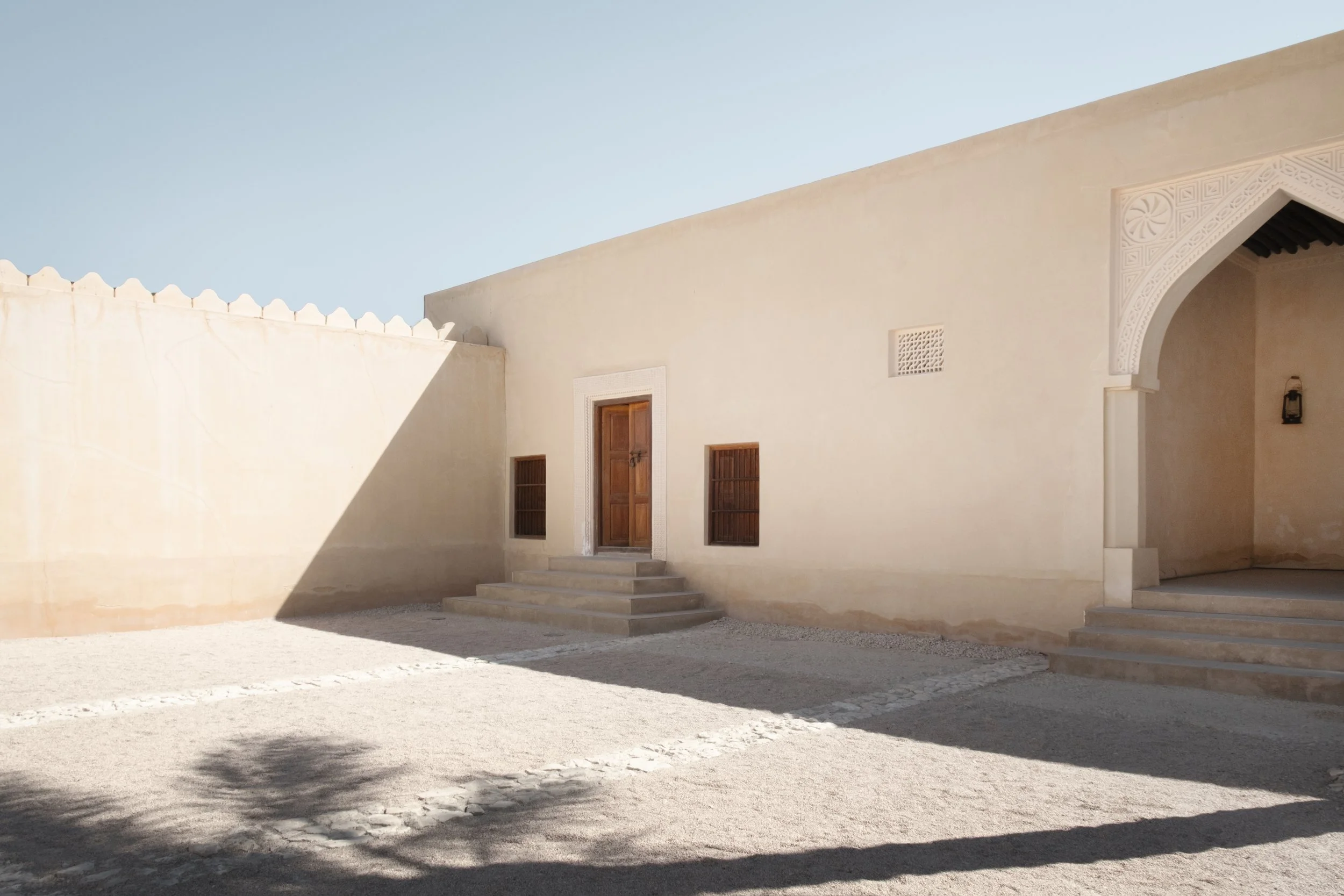 Courtyard of the heritage palace at the National Museum of Qatar in Doha, featuring minimalist sand-colored walls, wooden doors, and traditional Gulf architectural details under bright desert light.