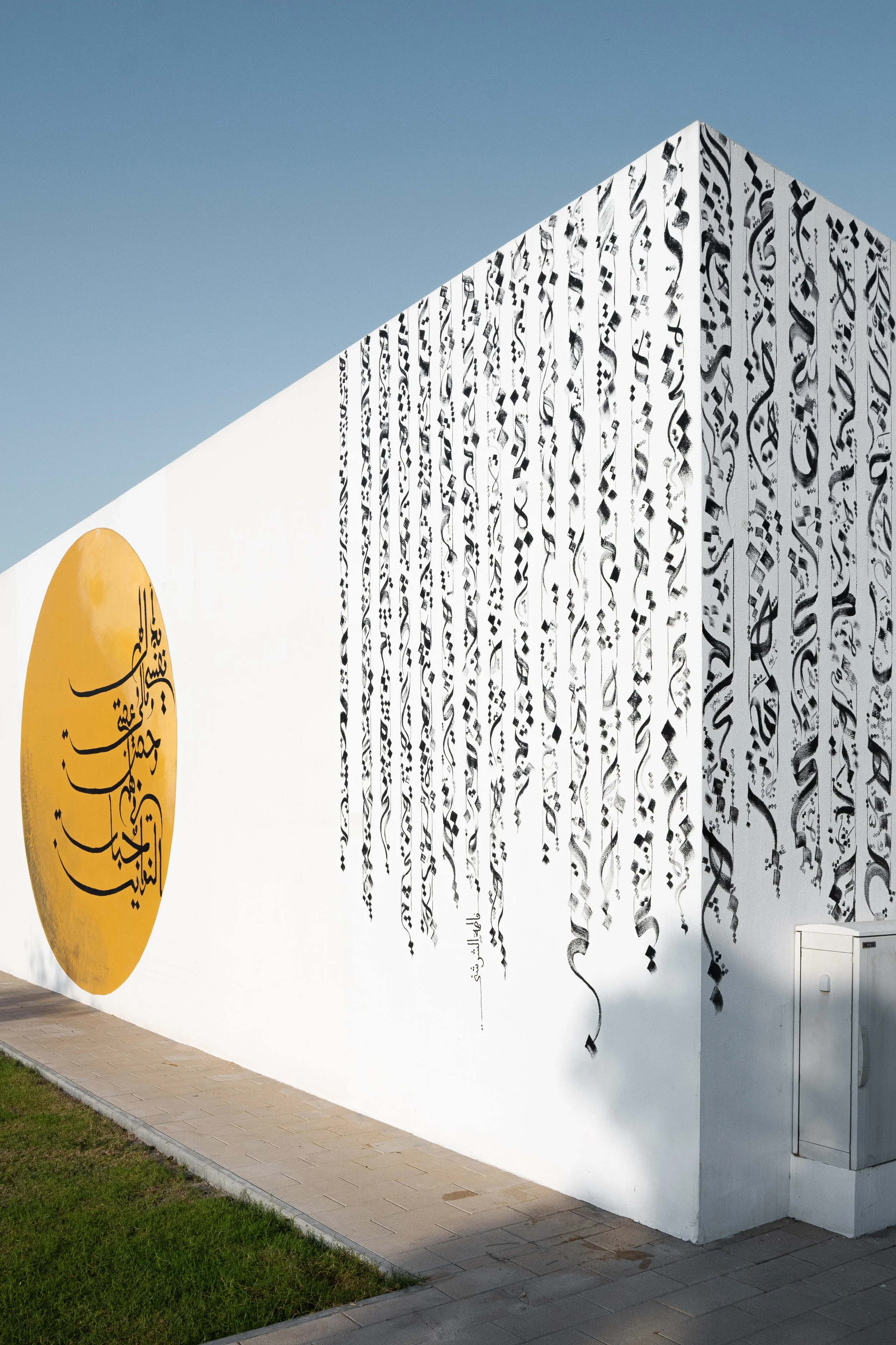 Angular perspective of an art installation featuring cascading black Arabic calligraphy and a yellow circular motif on a white wall in Qatar.