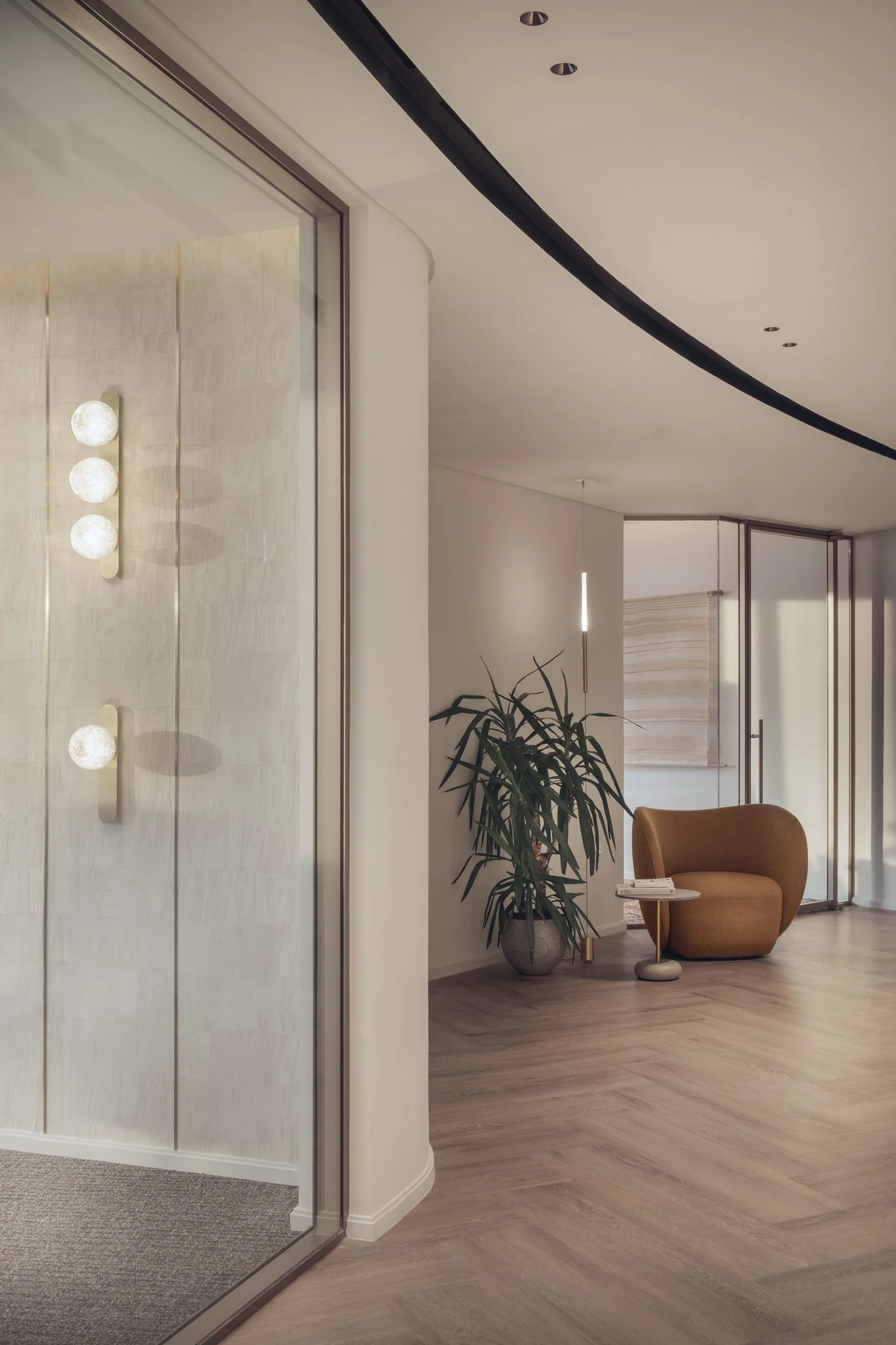 Architectural photography of curved office corridor in Tornado Tower, Doha. Herringbone wood floor, glass partitions, wall sconces, and lounge seating. Interior design by Roar.