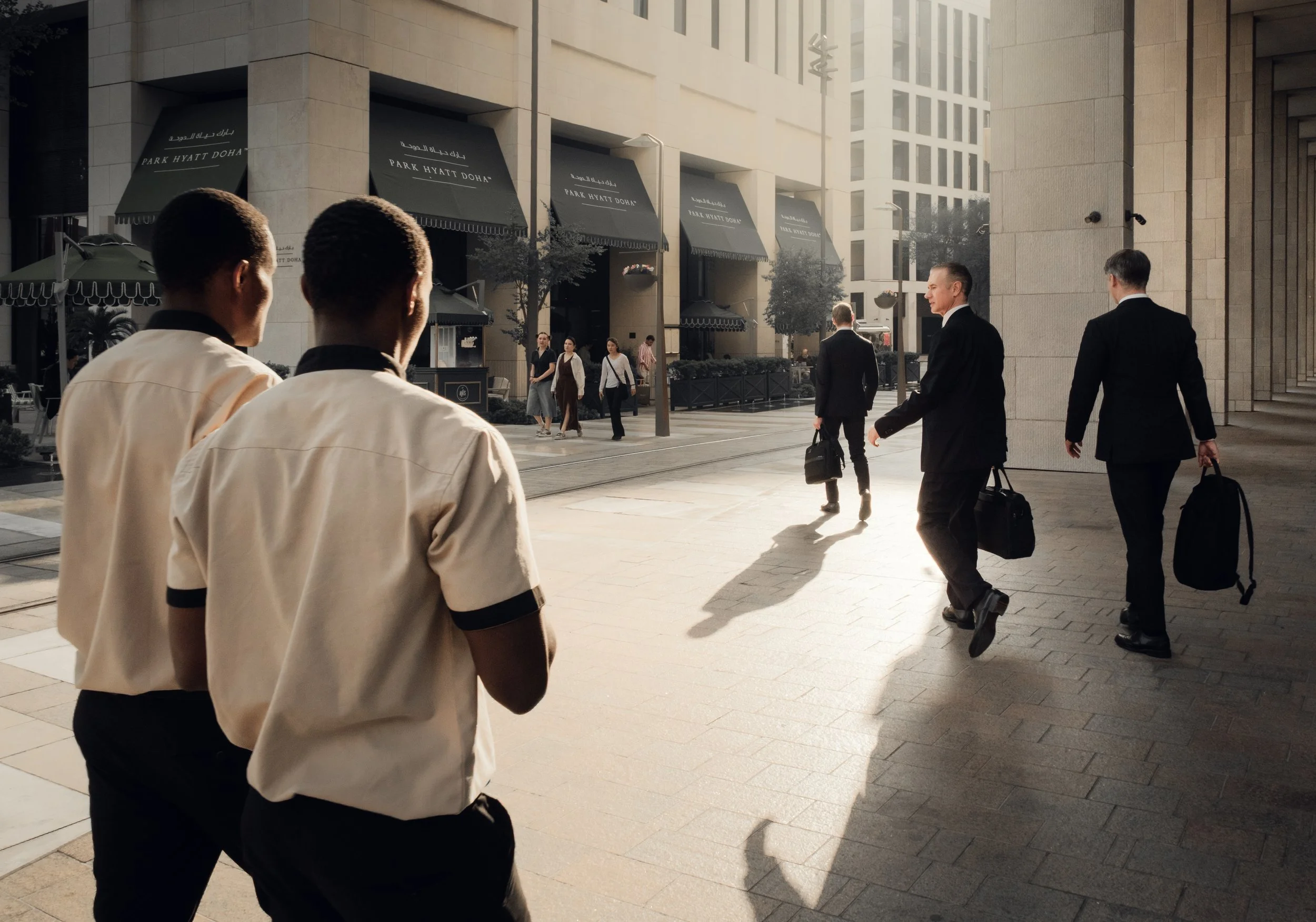 Pedestrians moving through a business district in Msheireb Downtown Doha, showing everyday urban life, formal architecture, natural light, and human scale within a walkable environment.