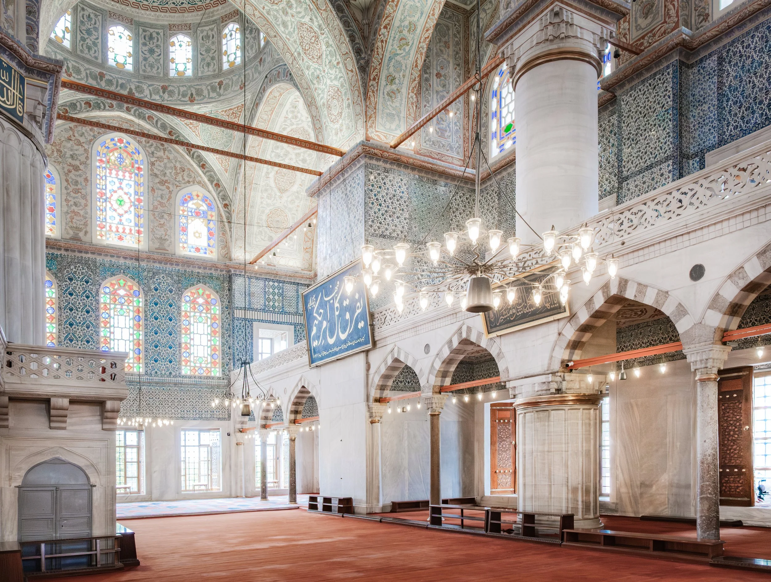 Wide interior view of the Blue Mosque in Istanbul with stained glass windows and chandeliers.