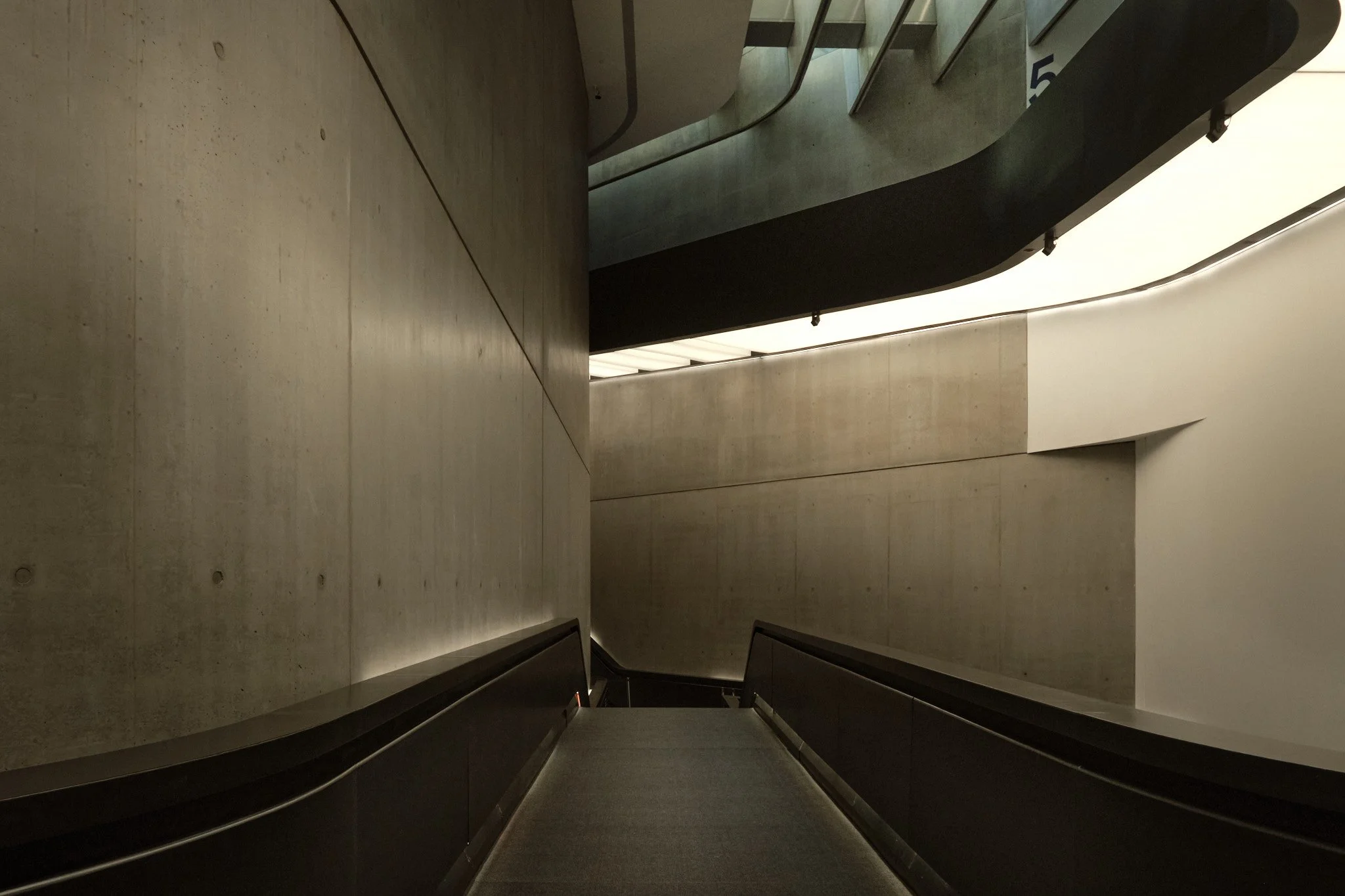 Interior corridor at MAXXI Rome with concrete walls close on both sides, spatial compression before the adjacent gallery opens.