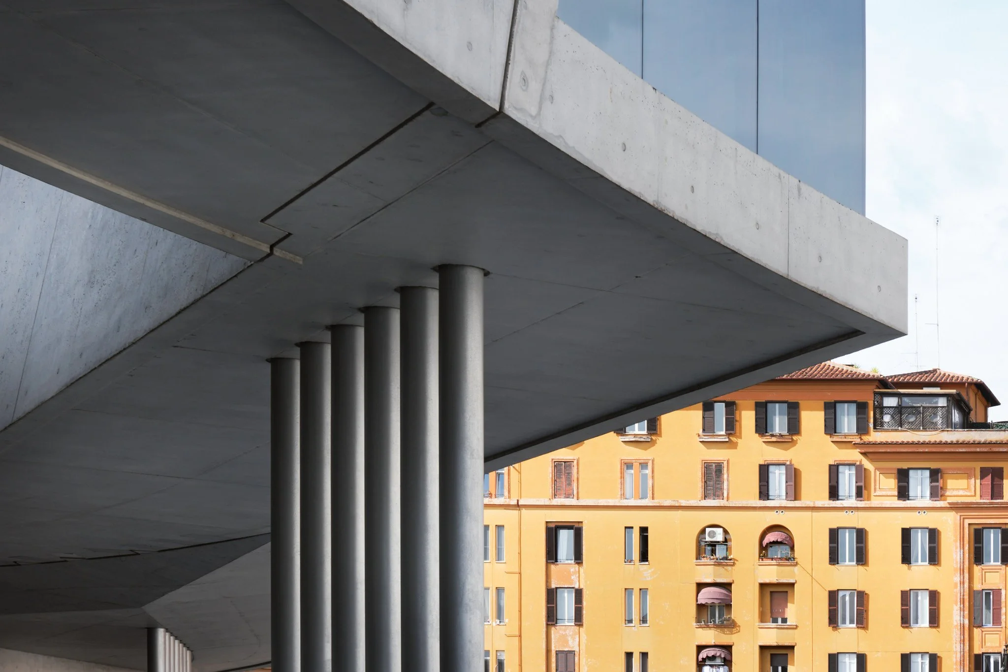 Exterior concrete columns at MAXXI Rome with the warm-toned buildings of the Flaminio neighborhood visible in the background, raw concrete against historic urban texture.