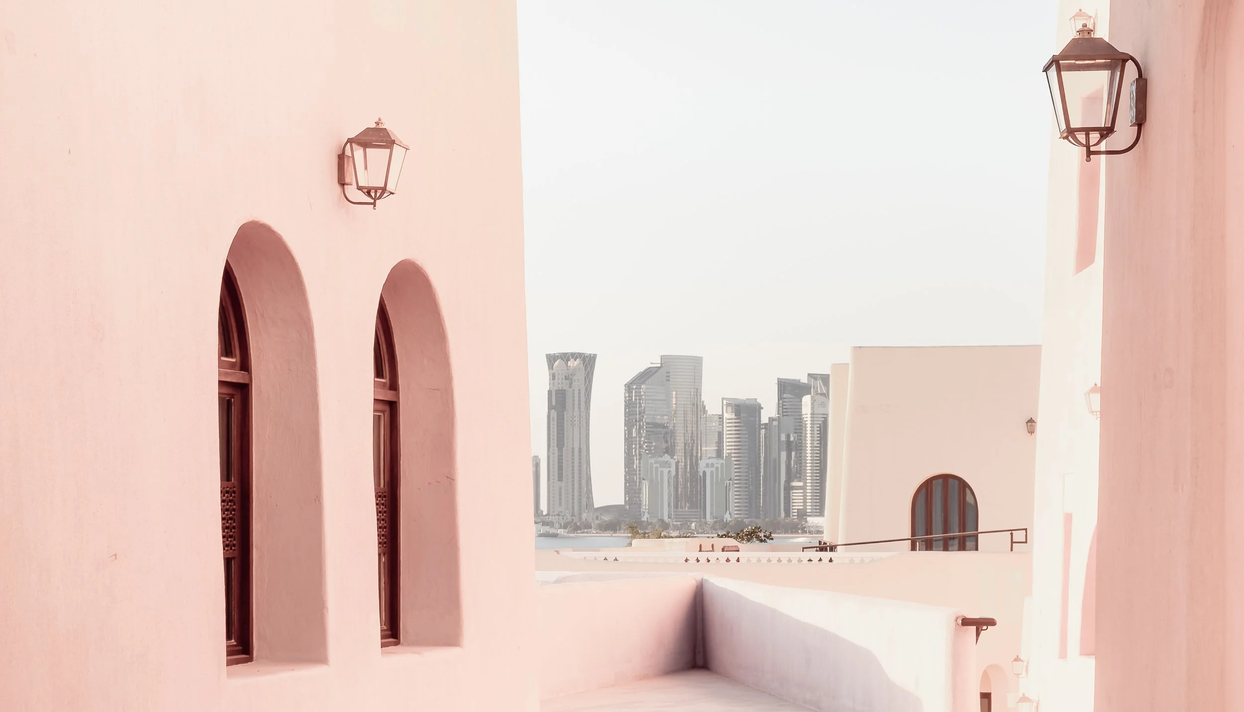 Pastel alley in Mina District, Doha, with West Bay skyline in the background.