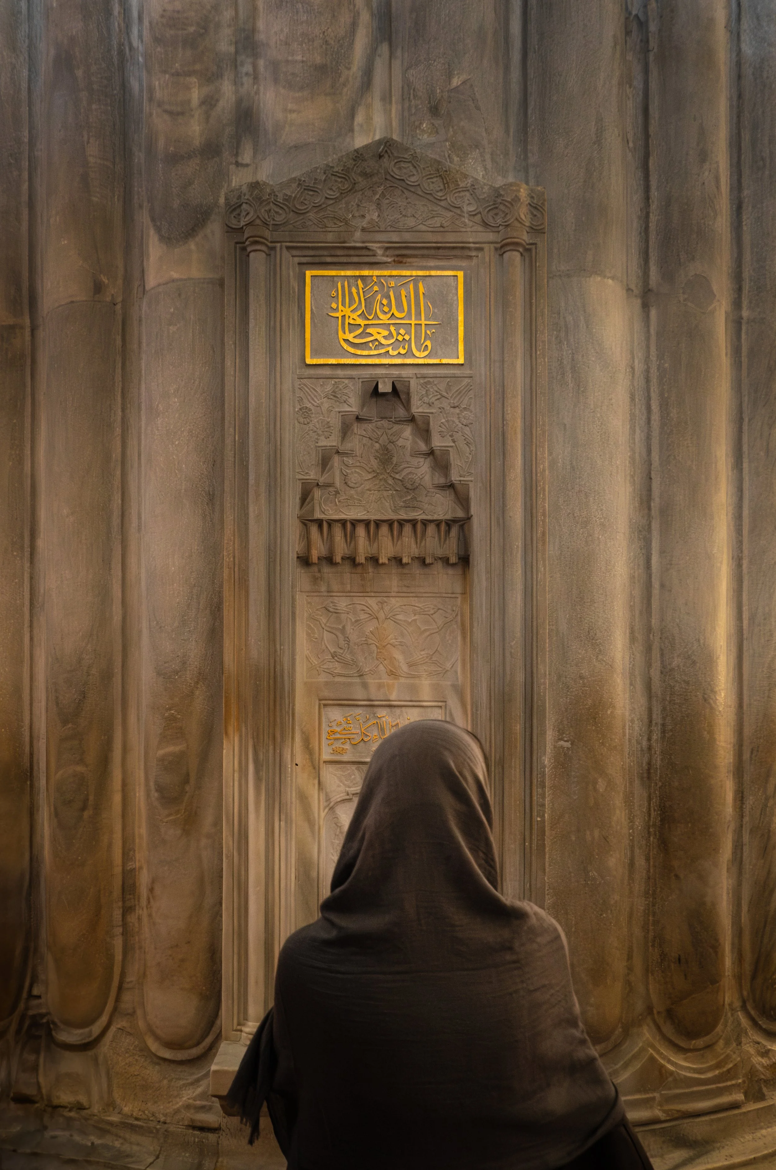 Woman in prayer seated inside the Blue Mosque in Istanbul near the mihrab.