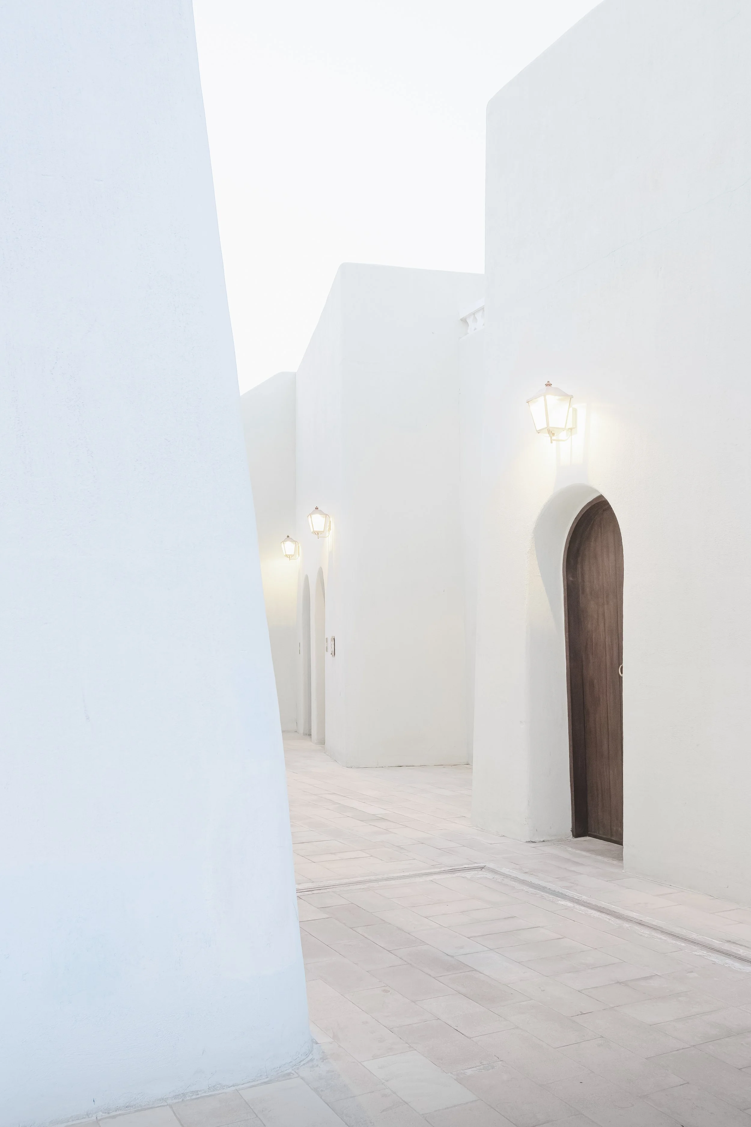 White and light blue pastel walls in Mina District, Doha, with arched doorway and lantern, photographed at dusk.