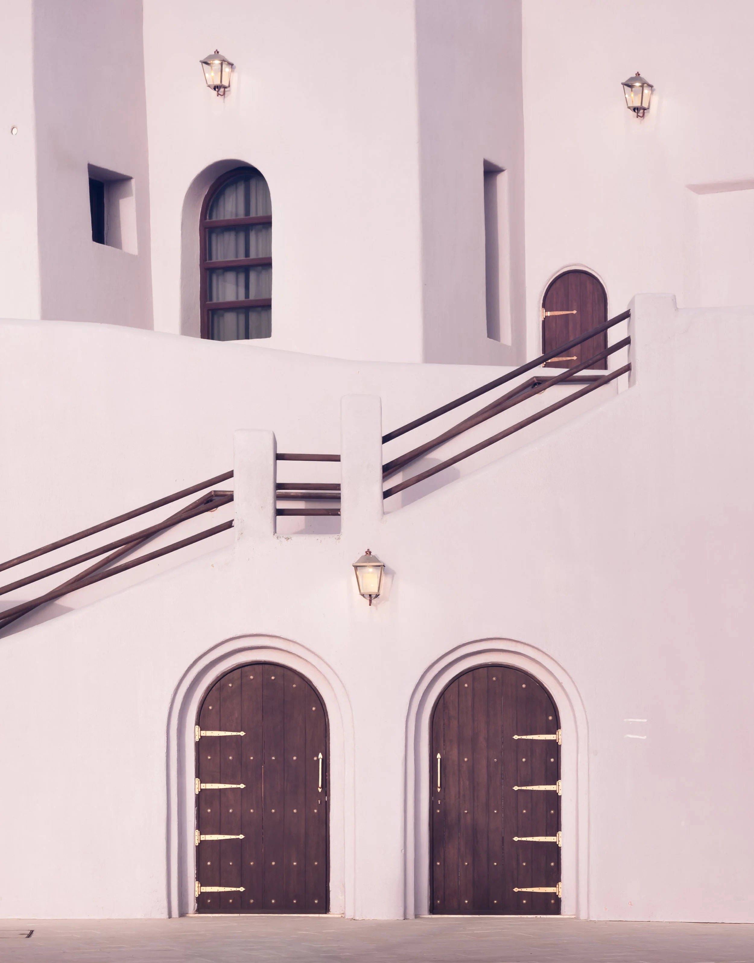 Double wooden arched doors with pastel pink facade and lanterns in Mina District, Doha, photographed in soft evening light.