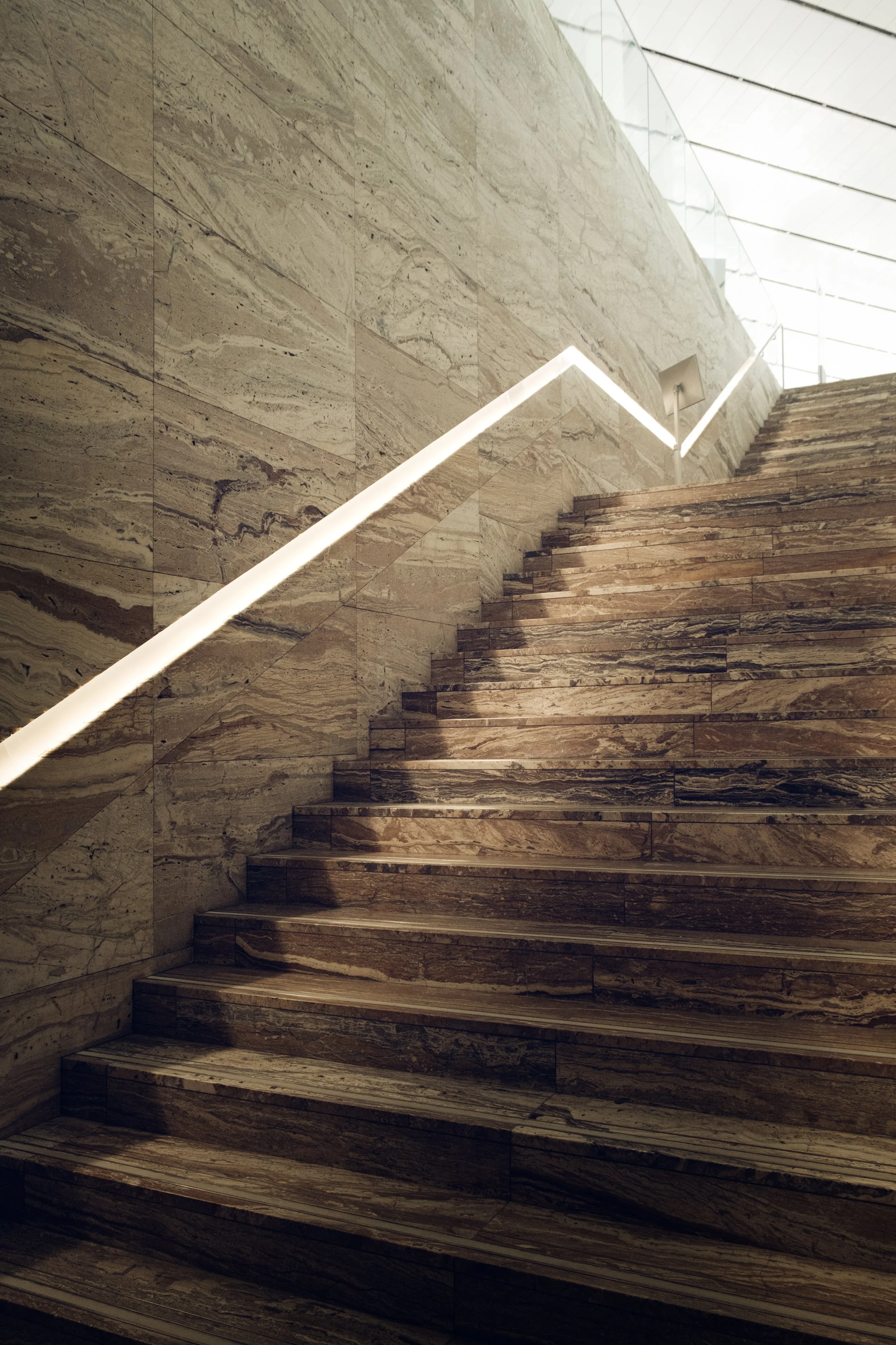 Interior photograph of the Qatar National Library showing a marble staircase with integrated linear lighting, highlighting material texture, geometric rhythm, and diffused natural light in Rem Koolhaas’s architectural design.