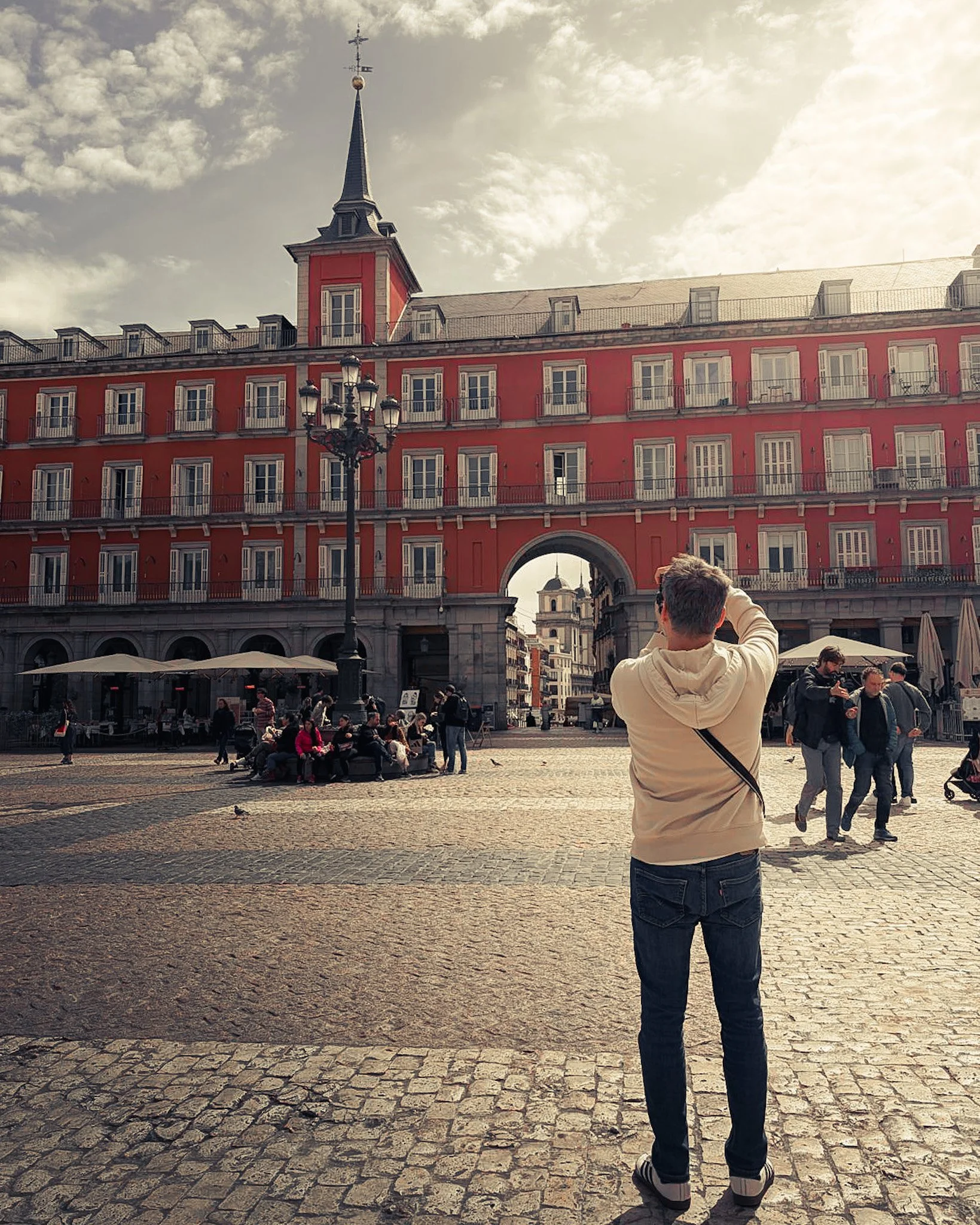 Architectural photographer Pedro Ferr framing a shot at Plaza Mayor, Madrid. Historic red facade with arched gateway and cobblestone square.