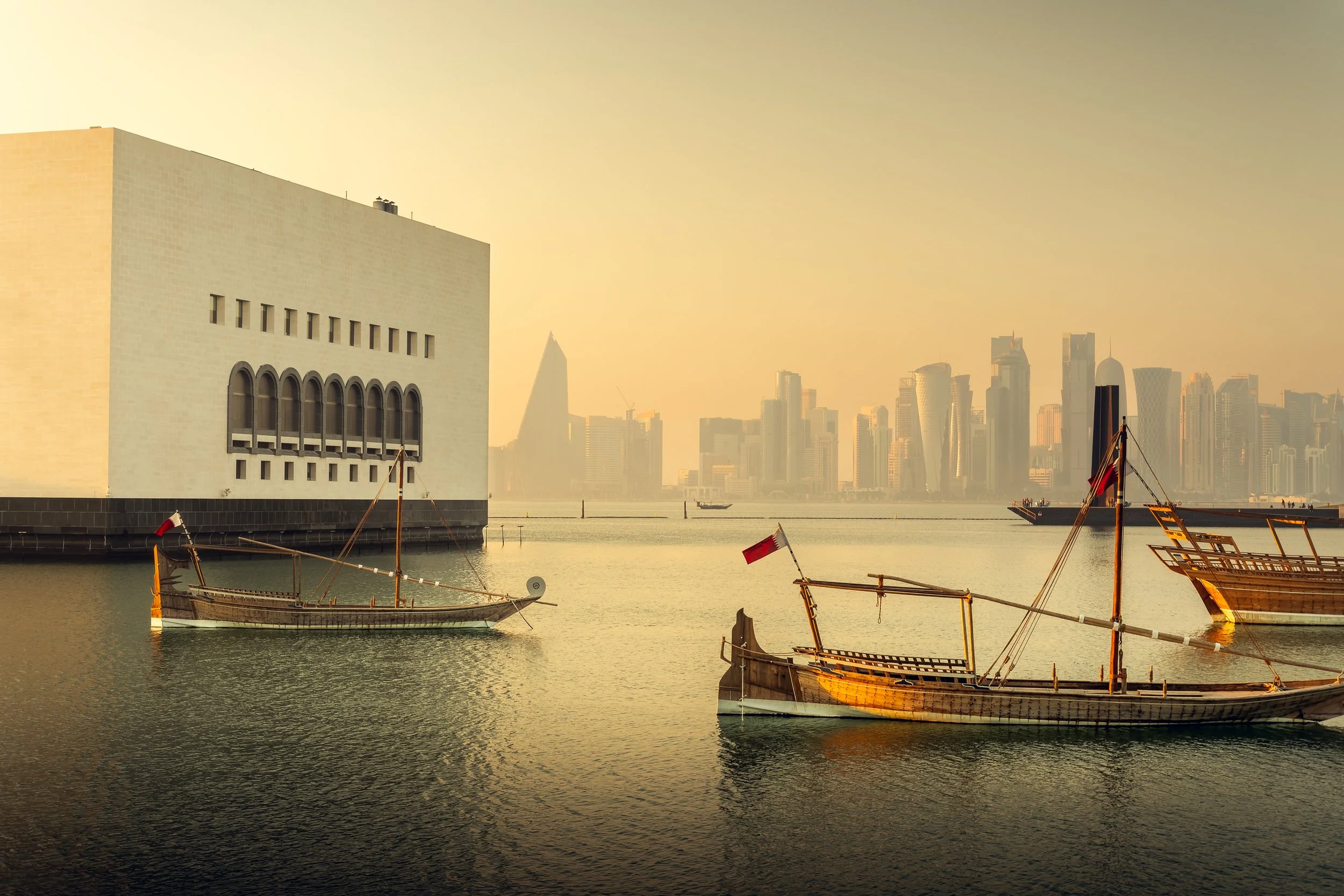 Museum of Islamic Art MIA exterior, Doha — view from the Corniche with traditional dhows and the West Bay skyline. Architectural photography by Pedro Ferr.