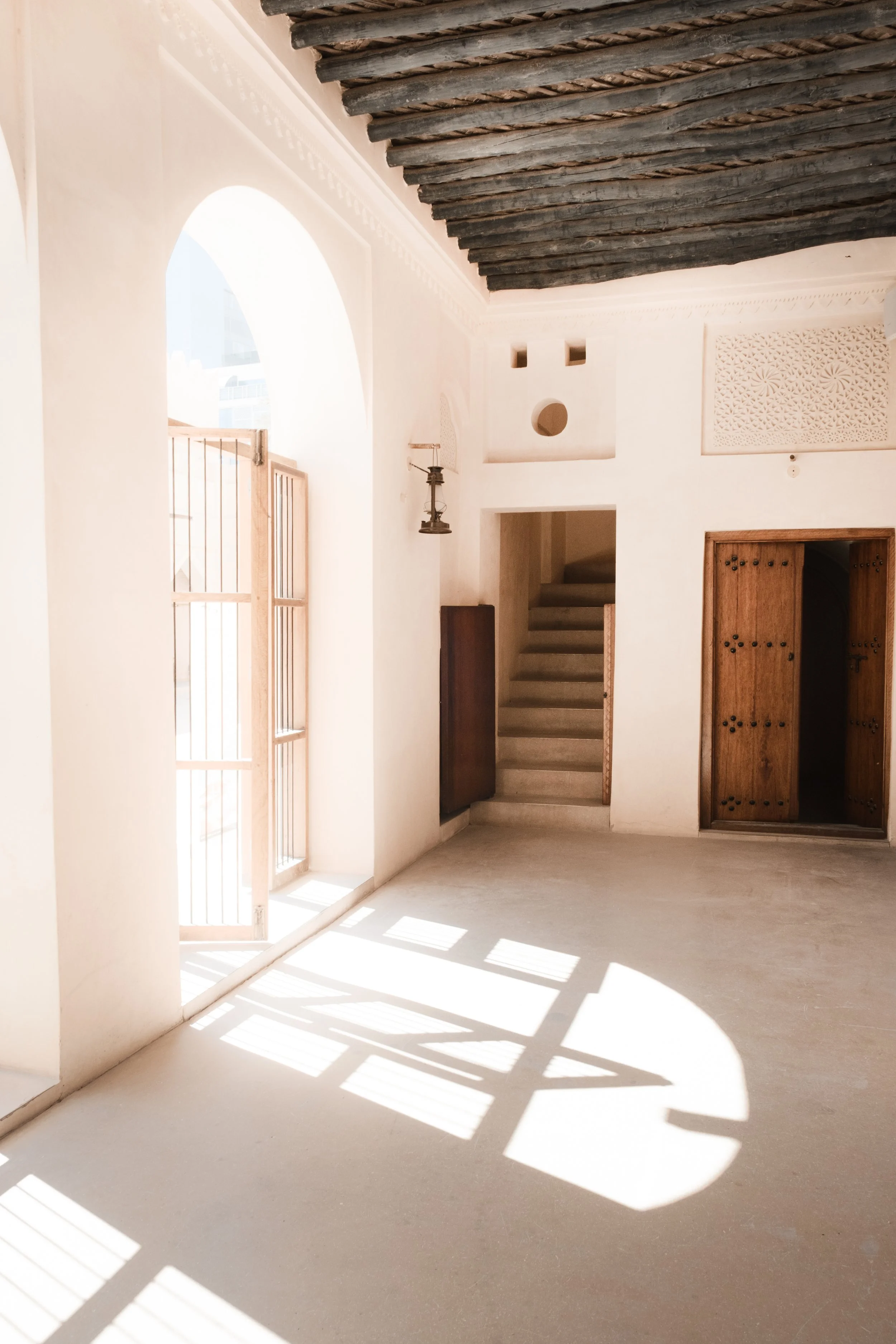 Sunlit interior of the heritage palace at the National Museum of Qatar in Doha, with wooden doors, traditional ceiling beams, and geometric light patterns on the floor.