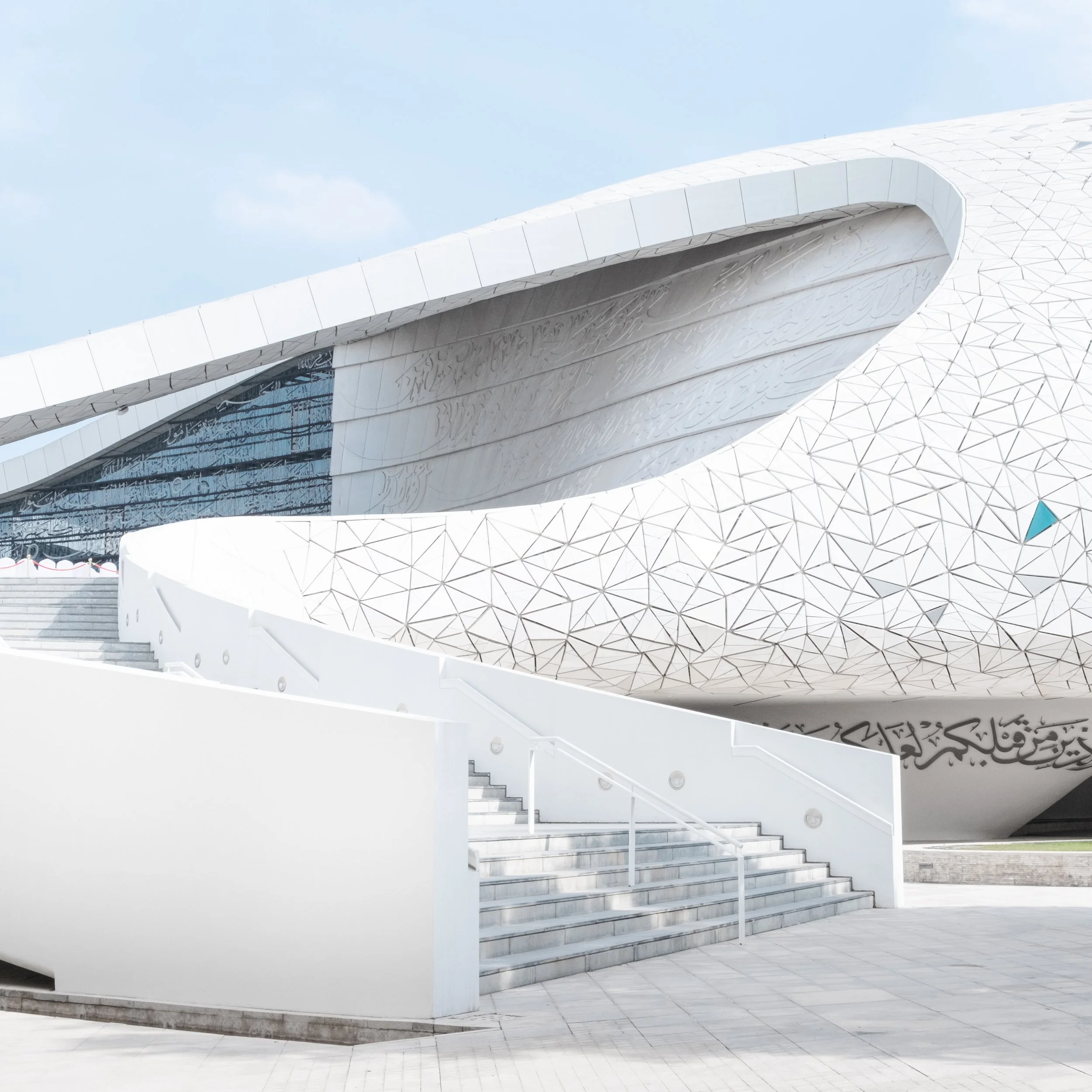 Exterior view of the Education City Mosque (Minaretein) in Doha, showing the white modern architecture, sweeping curves, geometric patterns, and stairs under a bright sky.