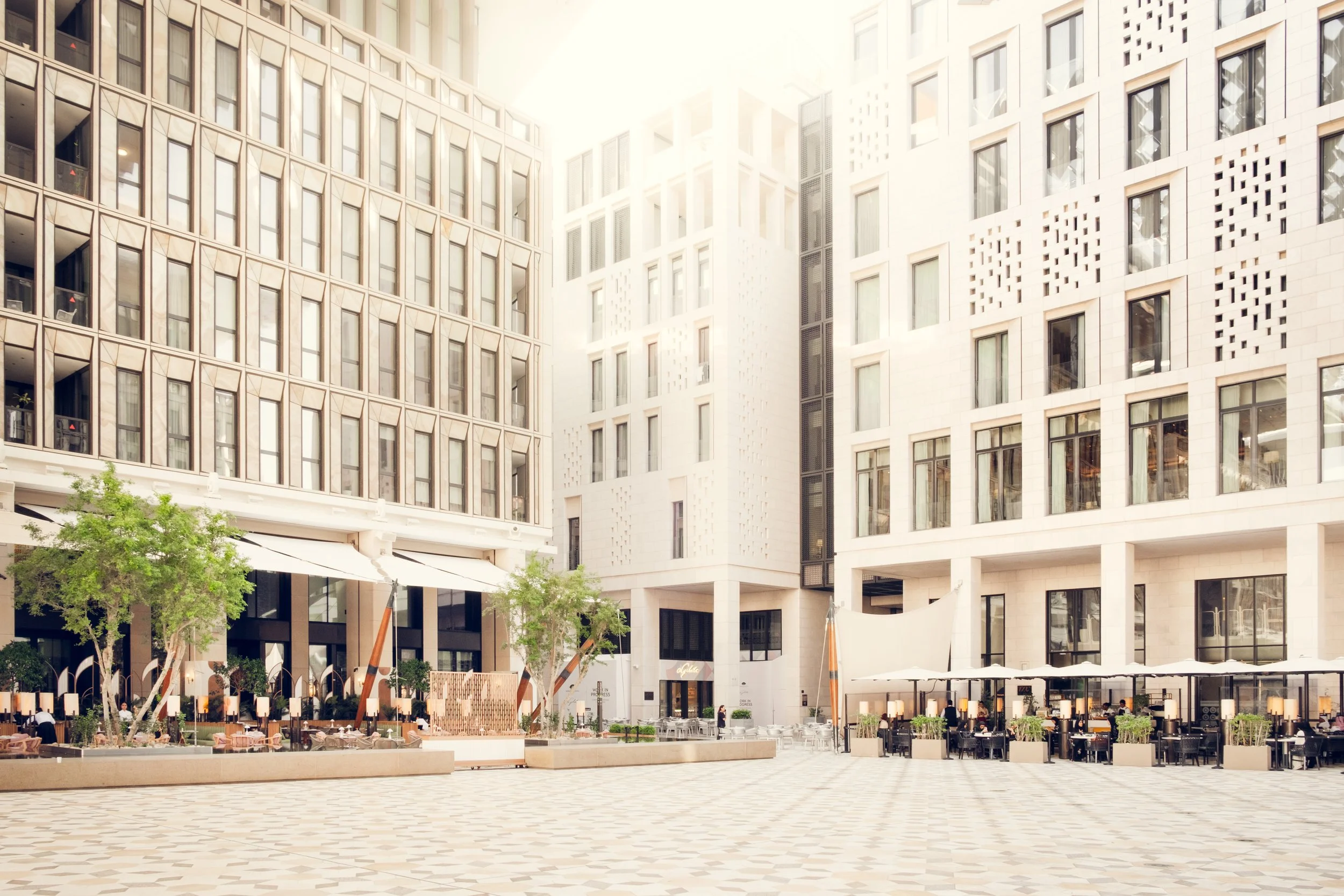 Wide view of a public square in Msheireb Downtown Doha showing mixed use contemporary architecture, outdoor seating areas, pedestrian focused design, and cohesive urban scale in natural daylight.