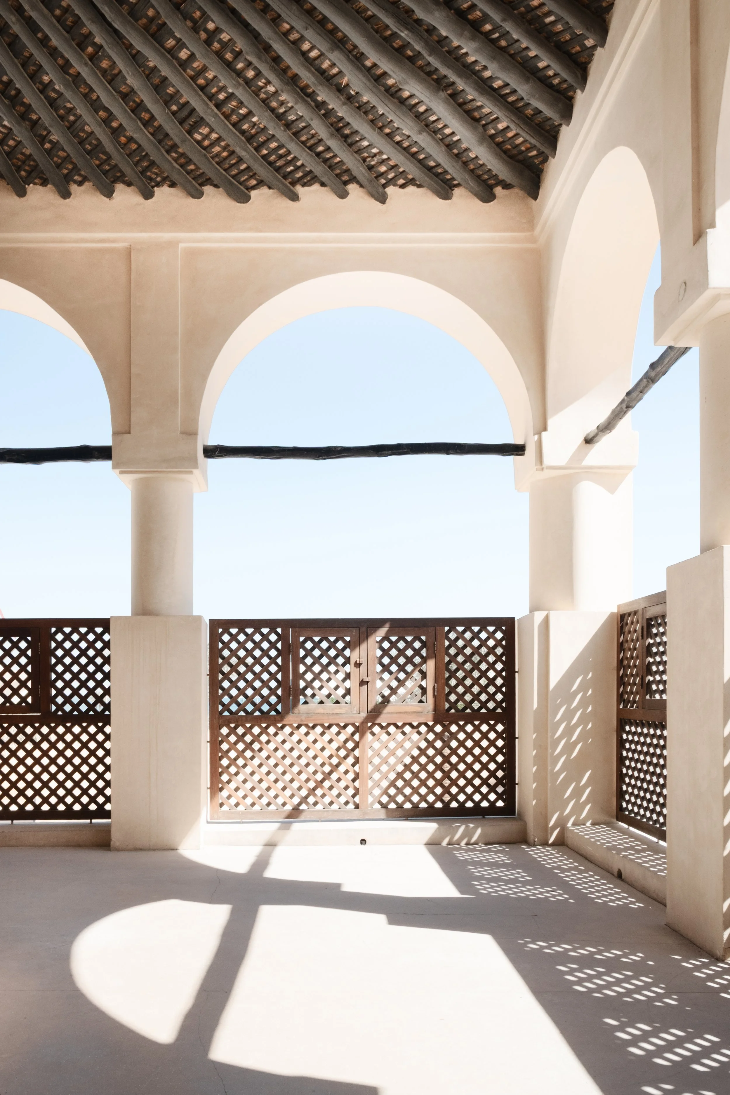 Arched balcony inside the heritage palace at the National Museum of Qatar in Doha, showing wooden lattice panels, traditional ceiling beams, and geometric light shadows.