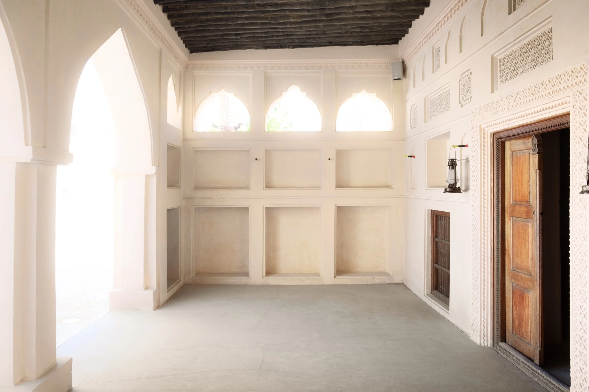 Interior of the heritage palace at the National Museum of Qatar in Doha, showing carved plaster details, wooden door, and filtered daylight that highlights Gulf architectural geometry.