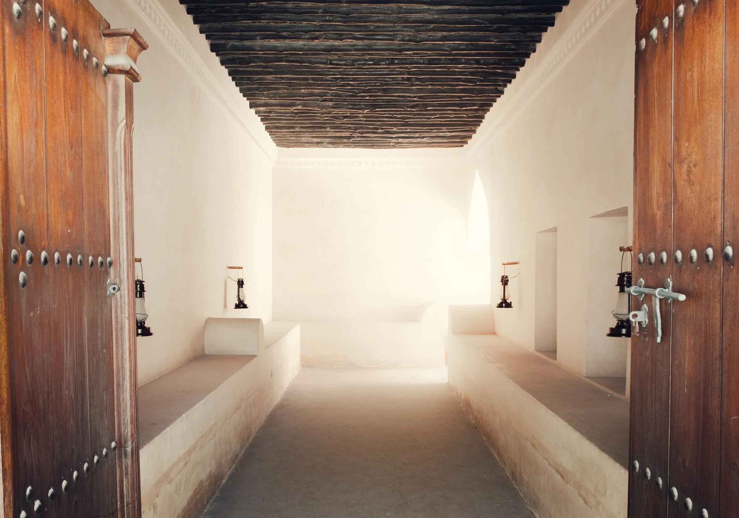 Interior room of the heritage palace at the National Museum of Qatar in Doha, showing traditional Gulf architecture with wooden ceiling beams, plaster walls, and soft desert light entering through an arch.