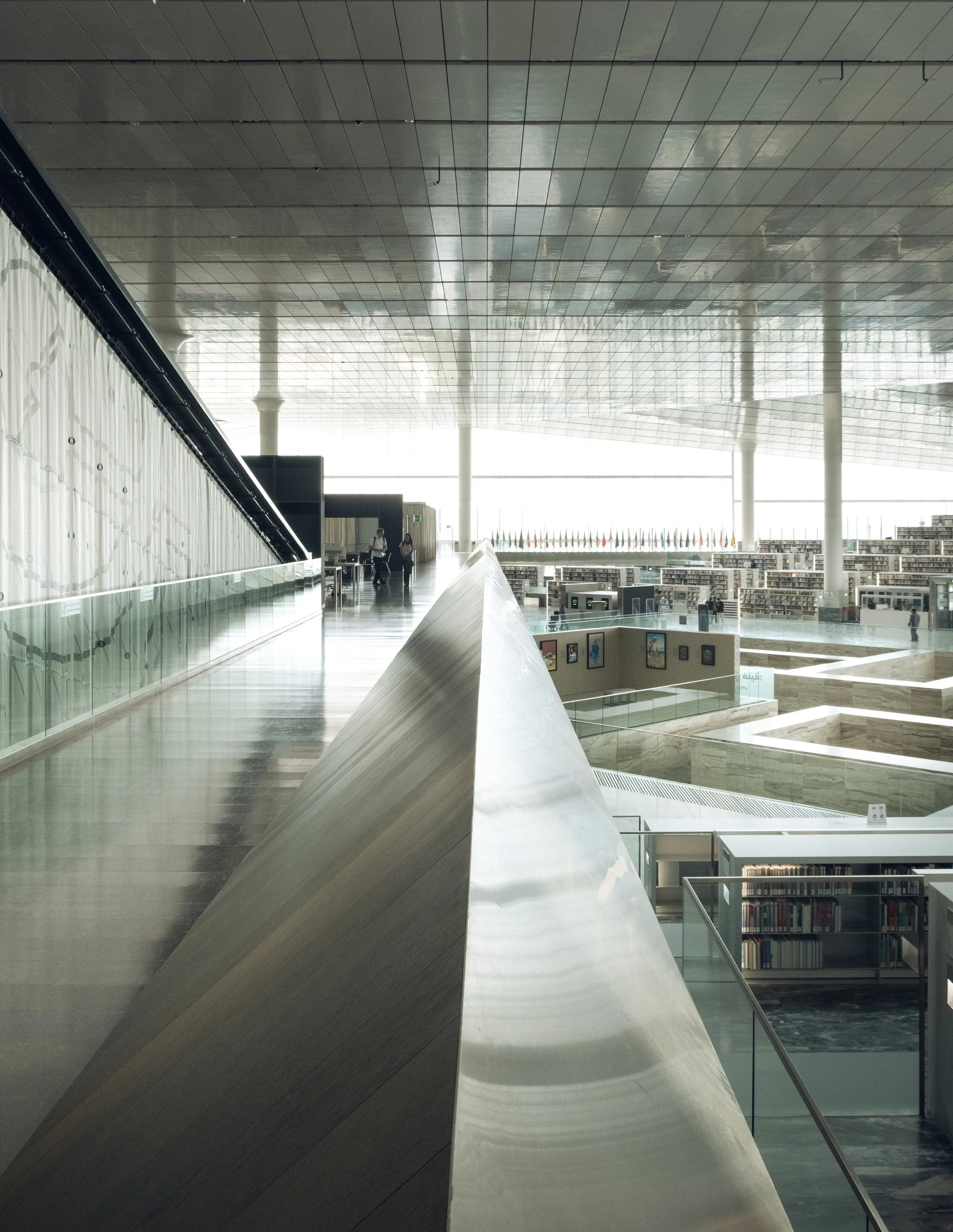 Interior view of the Qatar National Library showing the diagonal marble terrace and glass balustrades, with diffused natural light revealing geometric repetition and spatial rhythm in Rem Koolhaas’ architectural design, photographed by Pedro Ferr.