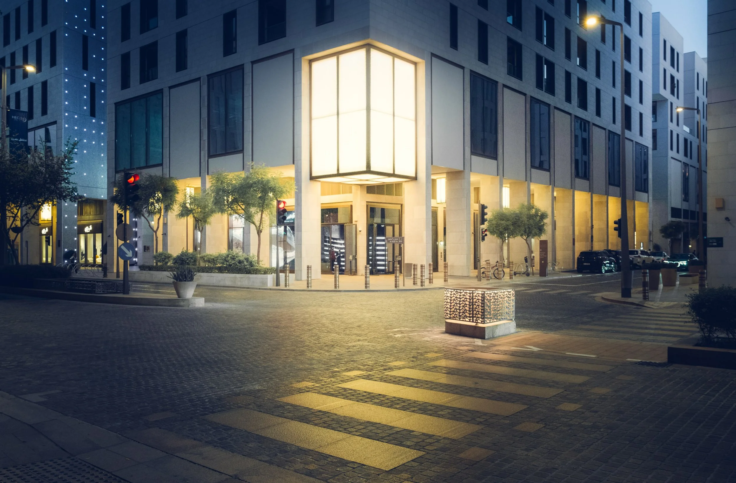 Intersection in Msheireb with a large illuminated cube volume at the corner of a modern building, warm interior light contrasting with the cool evening sky, clean lines and quiet streets that show Doha’s architecture at night for design and architect
