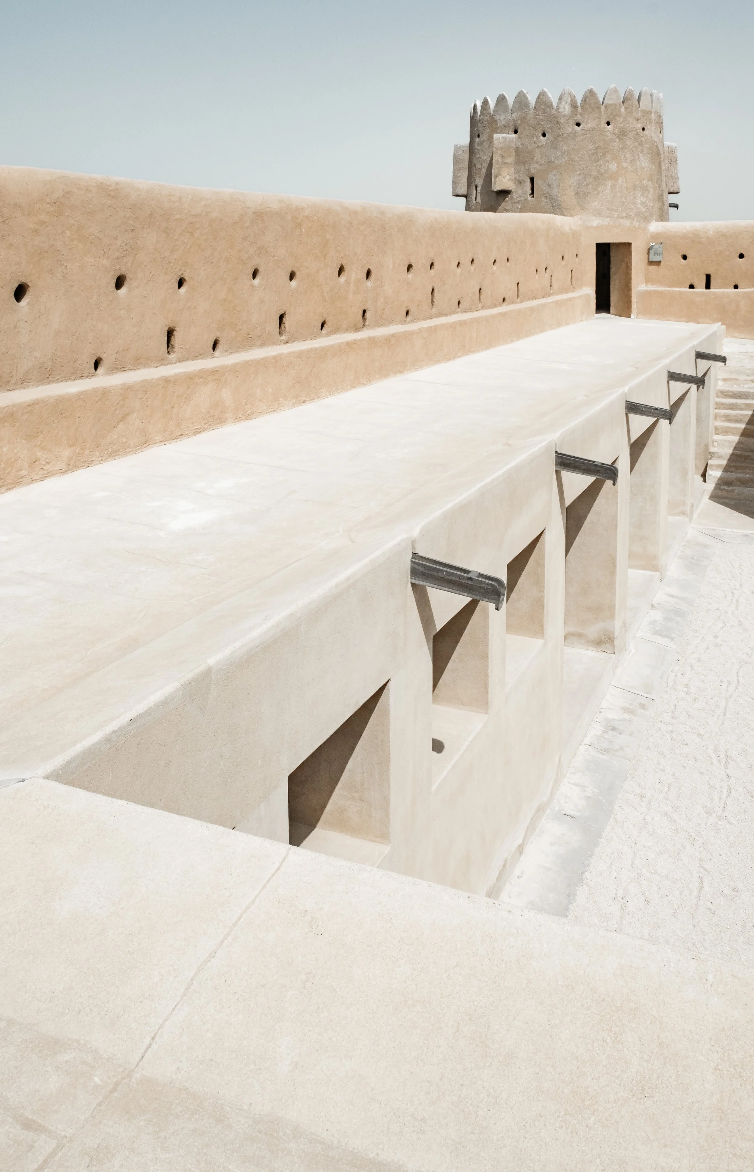 Perspective along Al Zubarah Fort’s crenellated wall walk, emphasizing defensive structure and shadow patterns, Qatar.