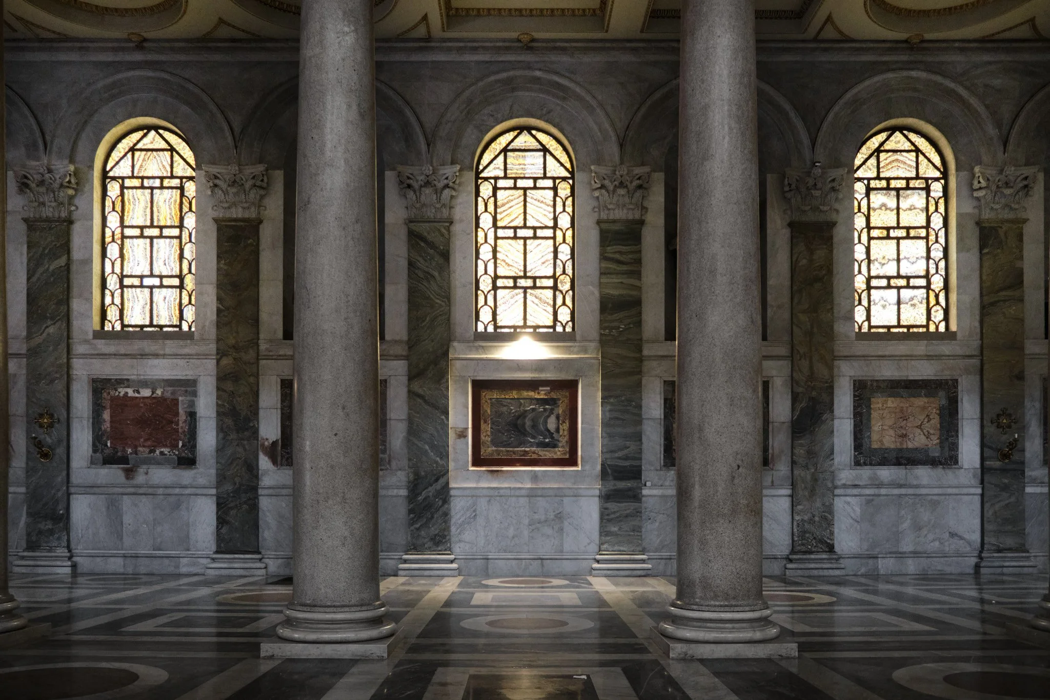 Interior of Basilica di San Paolo Fuori le Mura showing three tall arched clerestory windows with columns in deep shadow below, dramatic natural light.