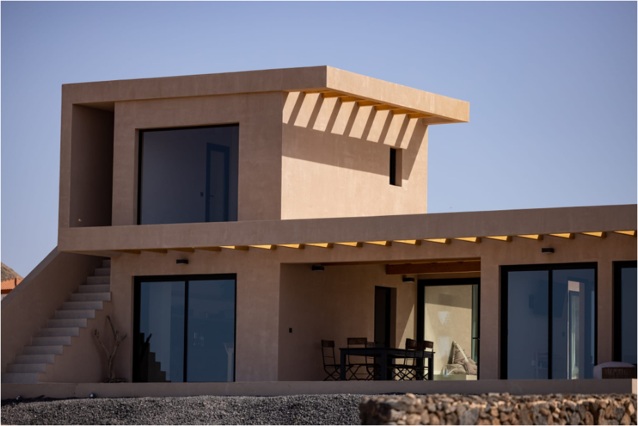 Casa moderna de dos pisos con paredes beige, terrazas abiertas, escaleras exteriores y ventanas de piso a techo.