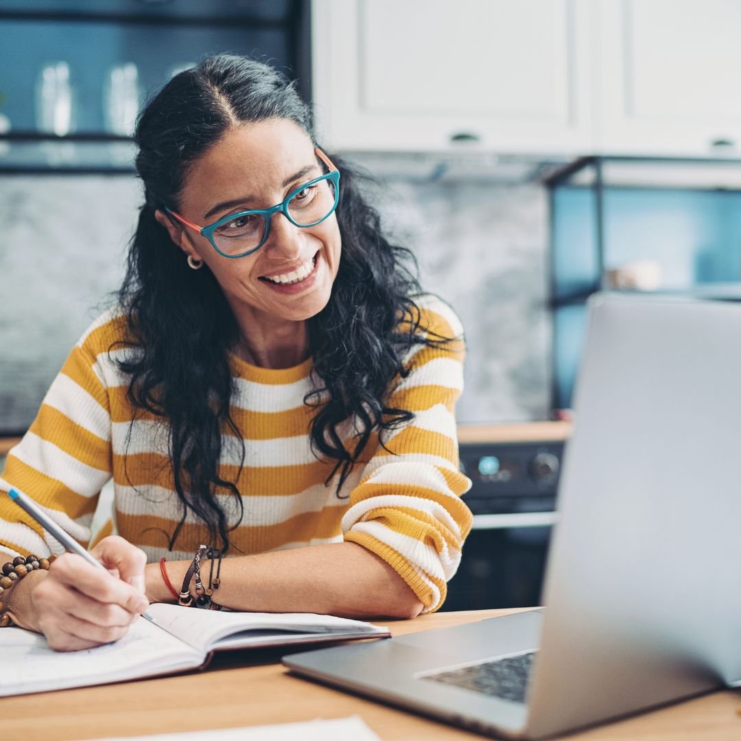 Smiling therapist sitting at her laptop and making notes while starting her private practice journey