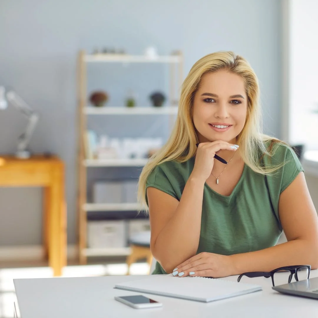 Confident therapist smiling at her desk with a laptop, symbolizing the relief and clarity the Starter’s Kit brings to starting a private practice in the Netherlands.