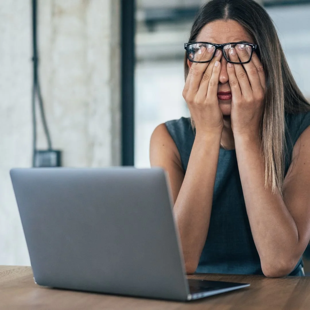 Exhausted therapist rubbing her eyes in front of an open laptop, symbolizing burnout, long admin hours, and sleepless nights in private practice.