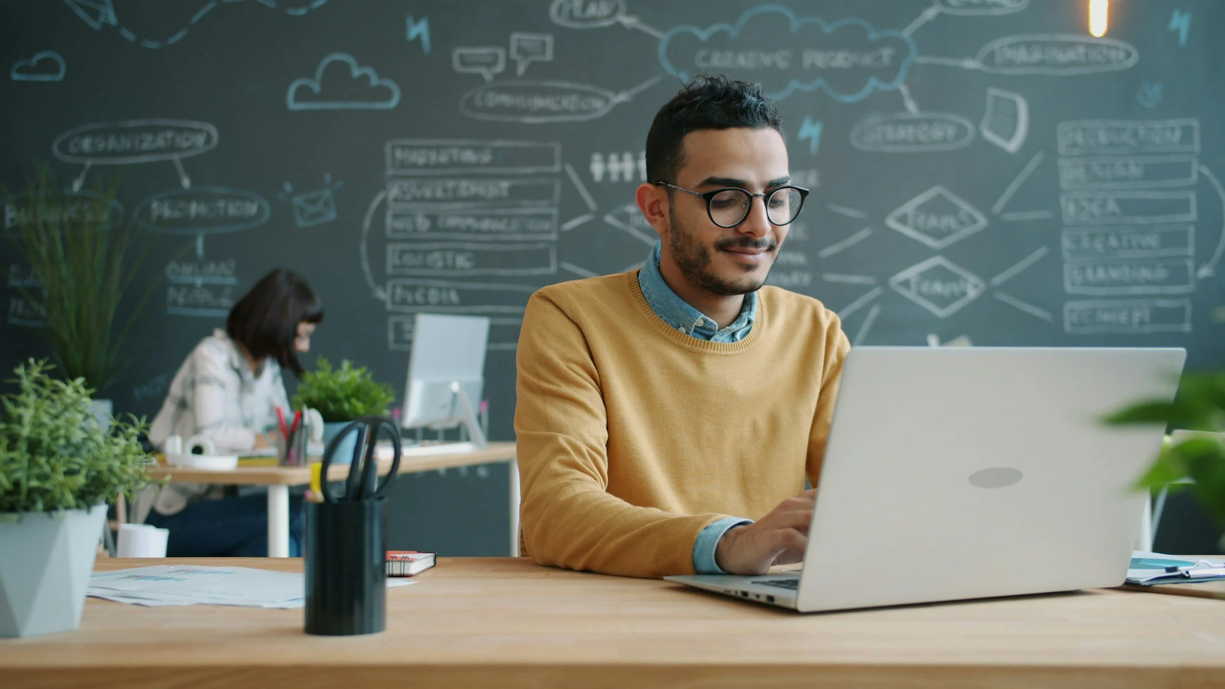 young man with glasses, yellow pullover sitting in front of laptop